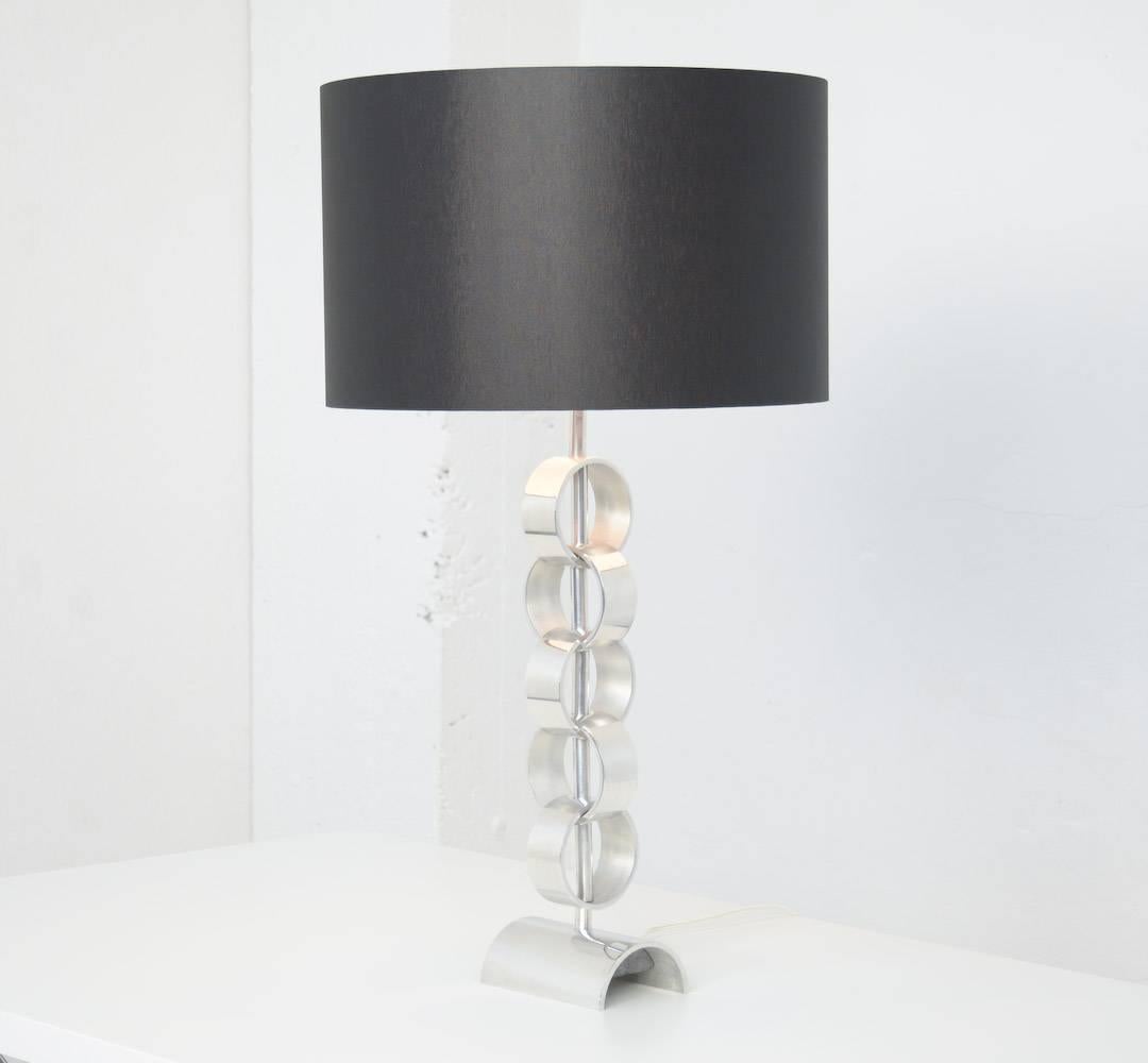 Cette belle lampe de table peut être datée des années 1970.
Il s'agit d'une lampe de table minimaliste et élégante composée de 5 anneaux chromés, enchaînés les uns aux autres.
Cette lampe est en parfait état, elle est recâblée et elle a un nouvel
