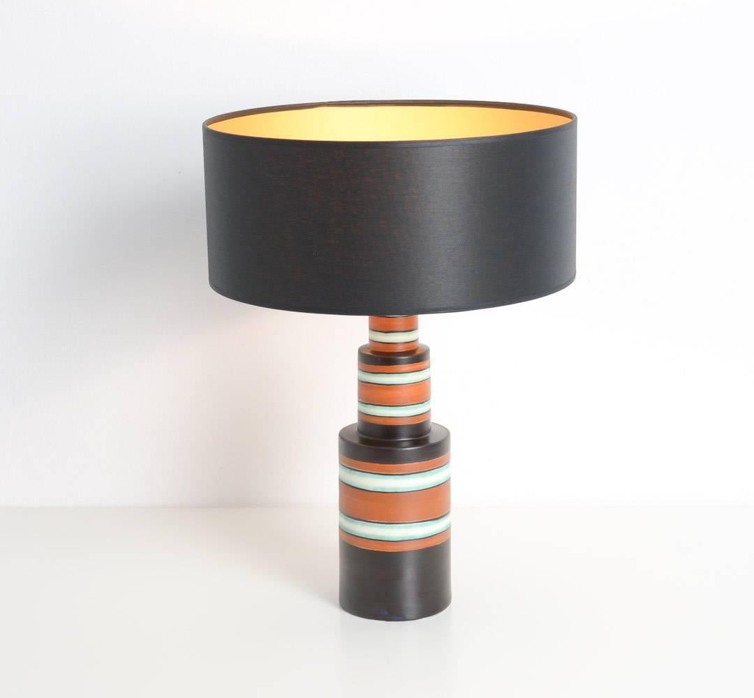 This Art Deco table lamp in matte enameled earthenware is decorated with a three-color geometric design with horizontal bands by the Atelier de Fantaisie.
This minimal table lamp is in perfect condition and marked. It has a new shade and it is