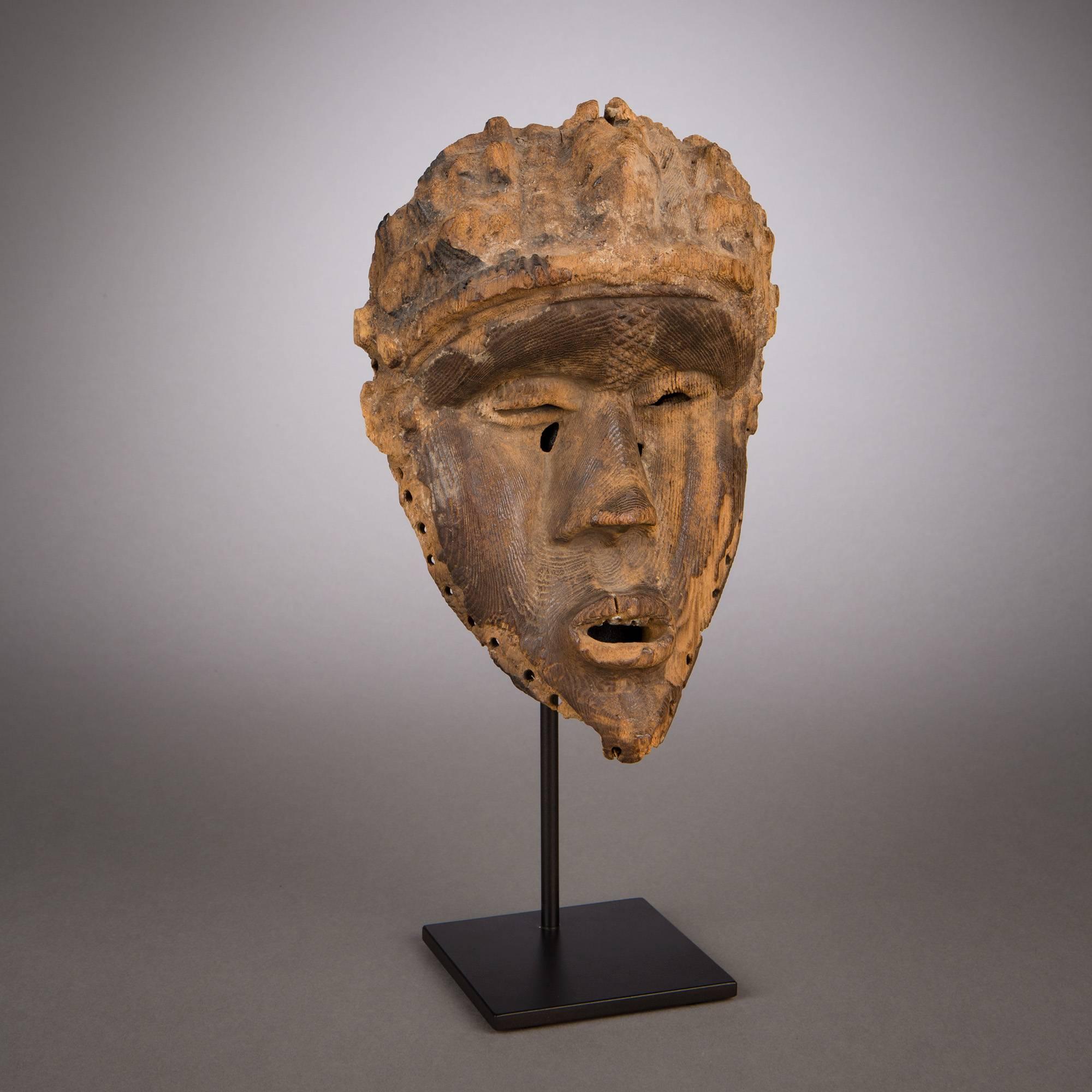 Bearing the deeply indented profile so Classic in Bassa masks, this superbly carved piece shows finely executed facial features, prominent cheekbones, and a jutting forehead surmounted by a coiffure. A vertical band of fine relief patterns runs up