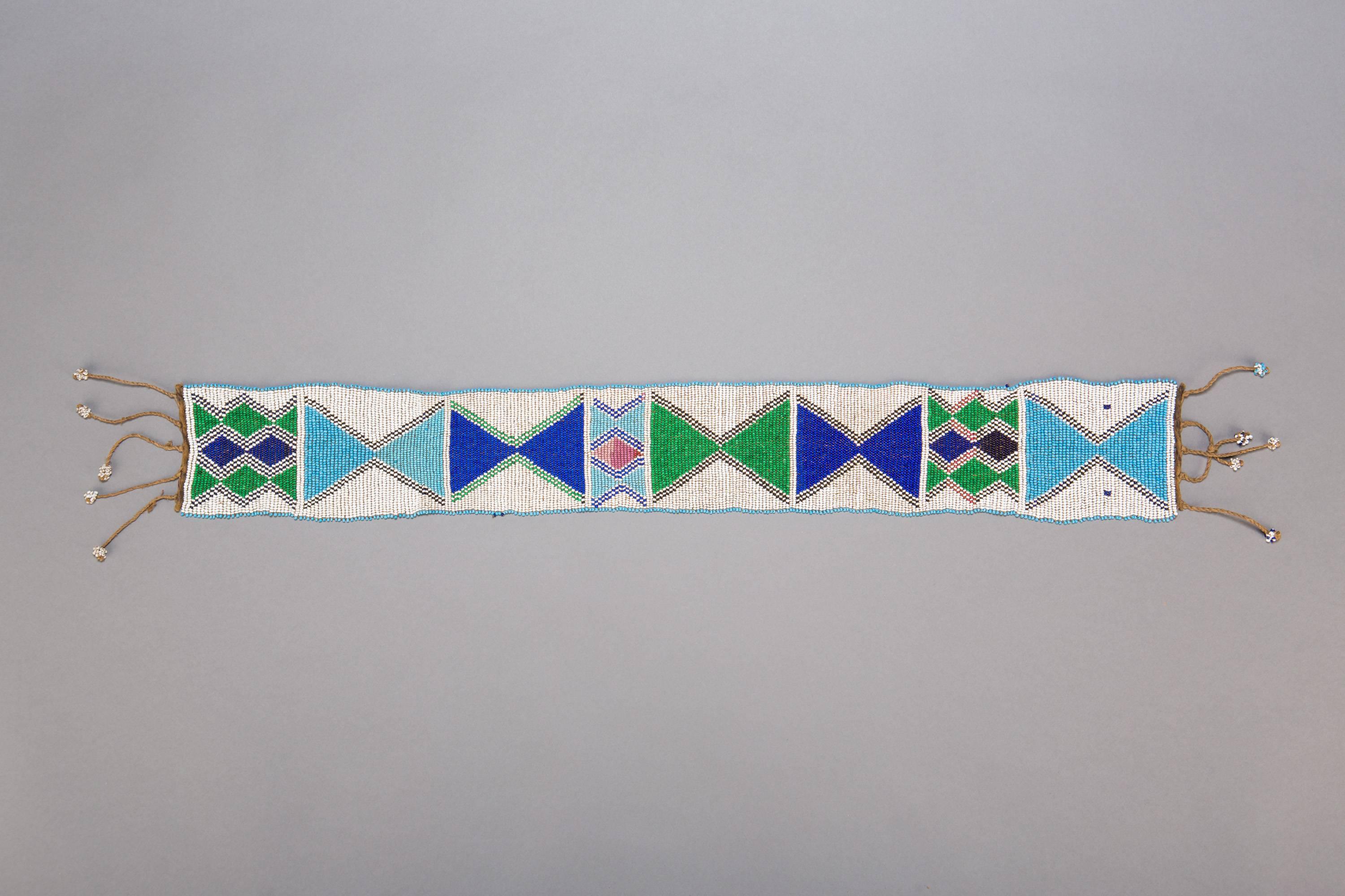 A lovely beadwork sash in white, green, and blue with delicate tassels at either end. Yao beadcraft commonly features triangular motifs, and this sash is no exception, featuring horizontally aligned sets of triangular forms joining in hourglass