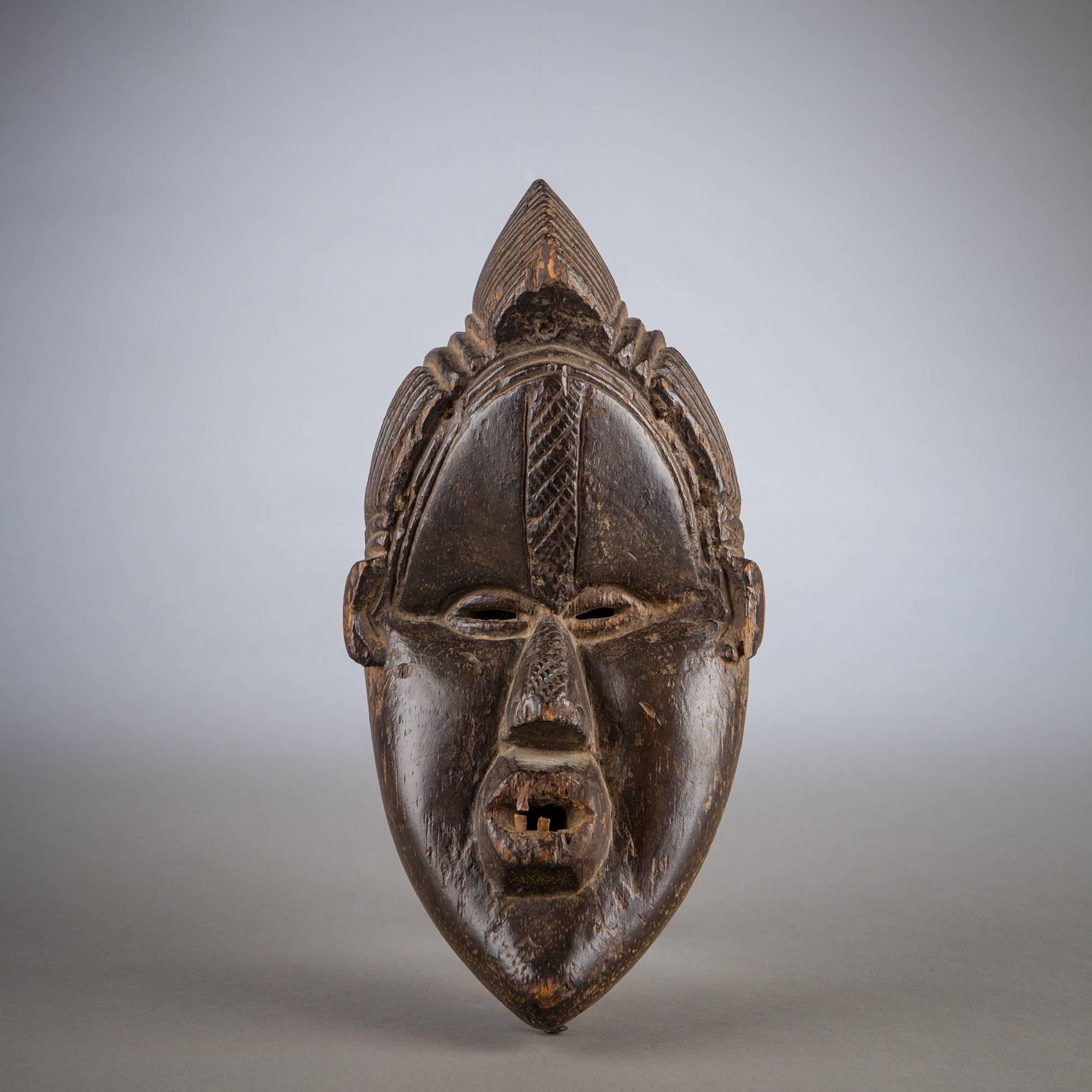 A great sense of mass imbues this Bassa mask, imposing with its classically large brow, full cheeks, and heavy, almond-shaped silhouette. As the face sinks forcefully in at the eyes, the nose and brow are projected dramatically outward, along with