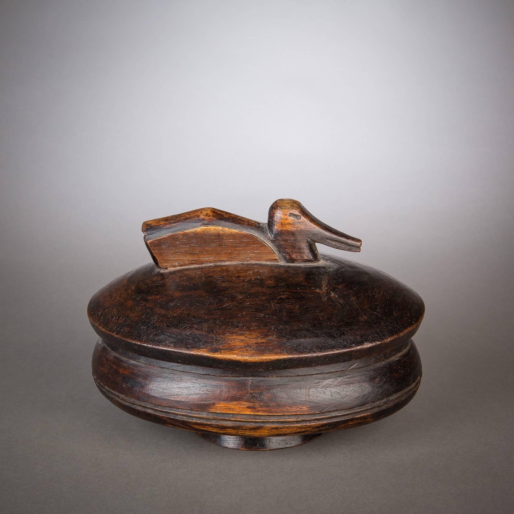 A beautifully carved lidded bowl with a decorative handle in the form of a swimming duck. This vessel is graced with a lovely, developed patina that displays deep, dark browns alongside warm umbers and honey-colored highlights.

The Lozi used