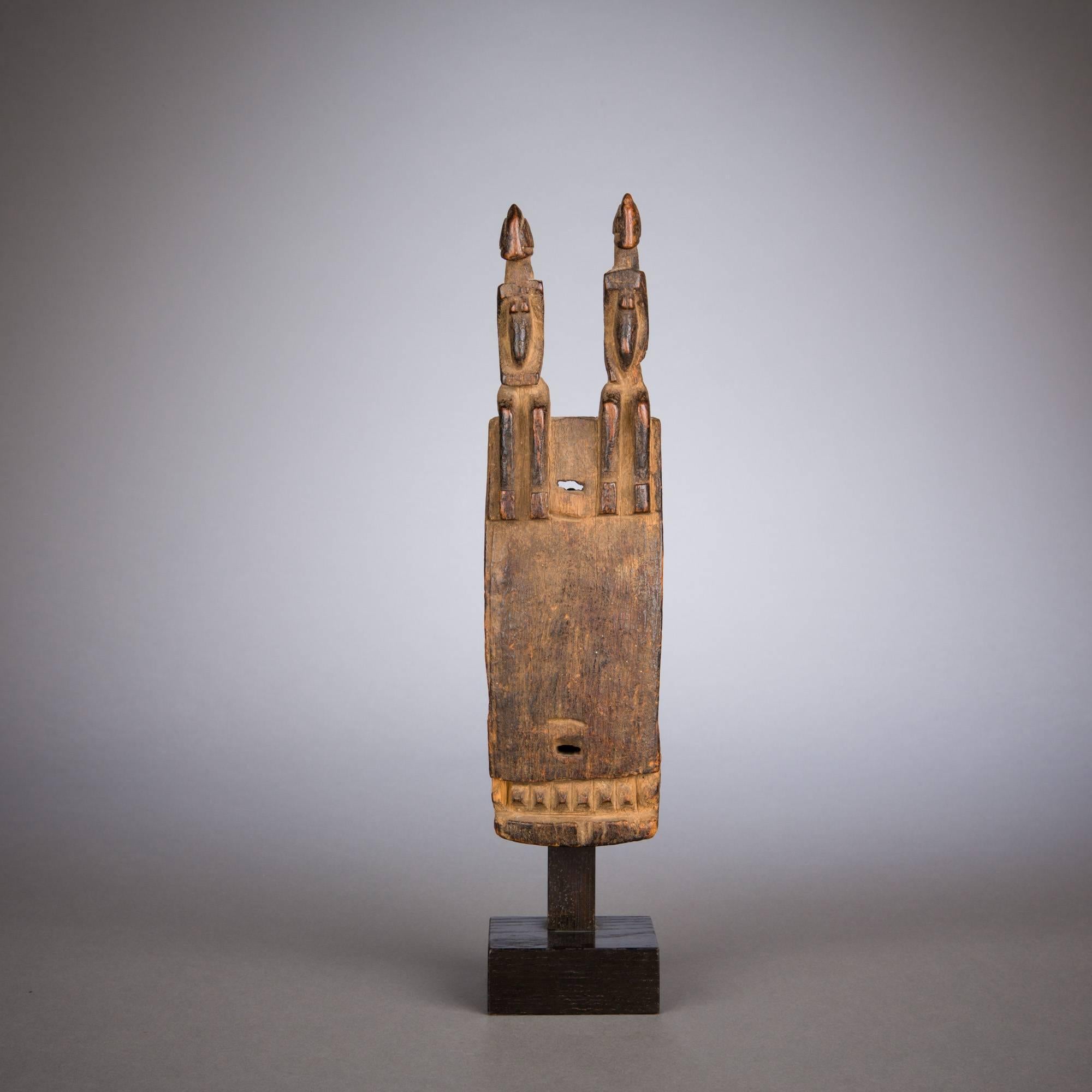 A fine Dogon door lock surmounted by two seated figures. The angular features of the pair are emphasized by strict rectilinear shapes, echoed at the bottom of the lock's face by a strip of projecting squares.

Used to protect houses and granaries,