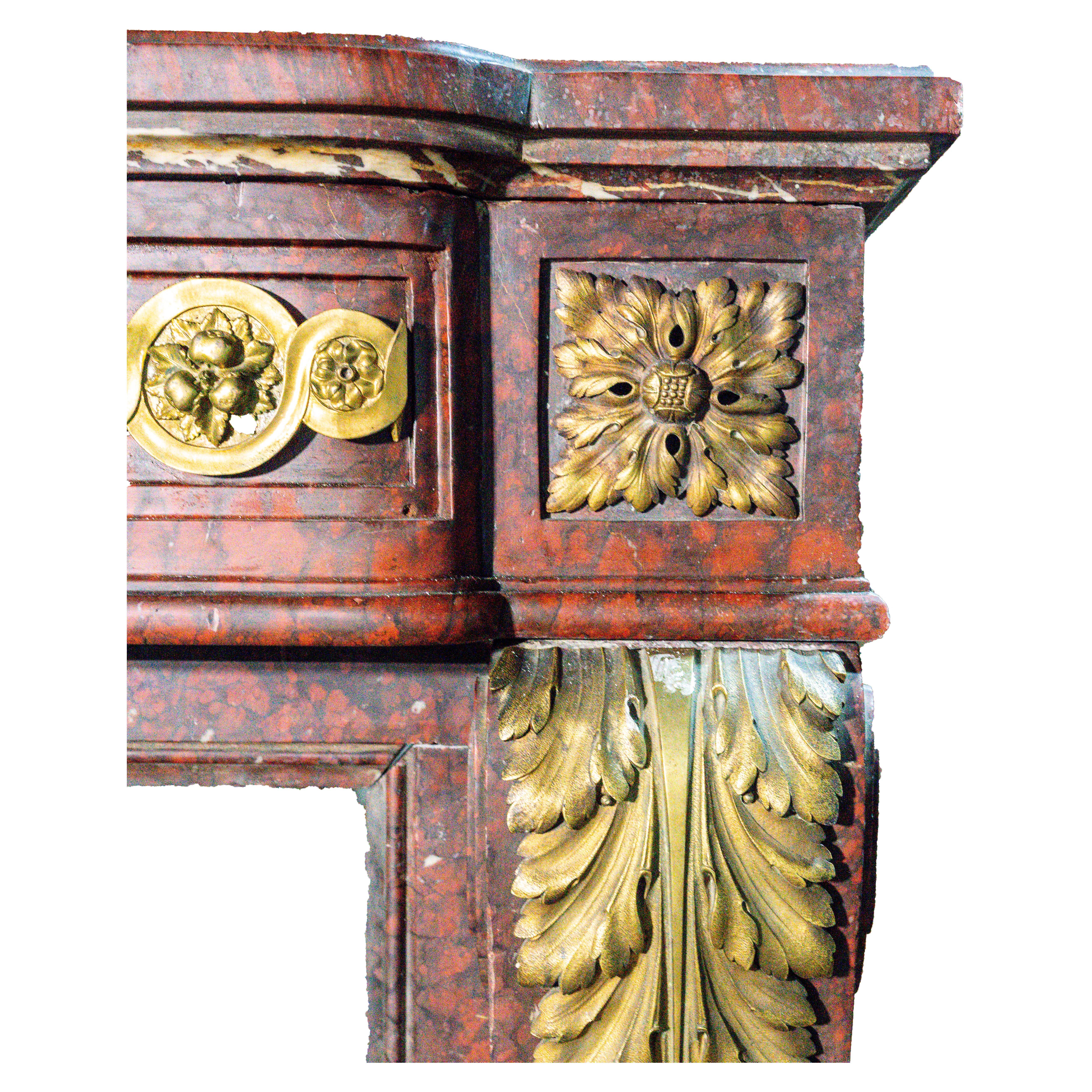 Un caminetto maestoso e riccamente decorato di epoca Luigi XVI, realizzato in squisito marmo rosso e impreziosito da decorazioni in ormolu finemente fuse e dorate. Le linee architettoniche sono esaltate da stipiti scanalati ornati da foglie d'acanto