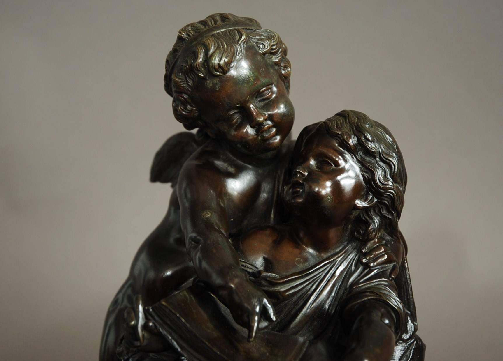 A French mid-19th century bronze of a putto (or cherub) standing next to a seated young girl. 

They are looking at or writing in a book, possibly symbolic of education and learning. 

They are depicted on a bronze naturalistic oval base with