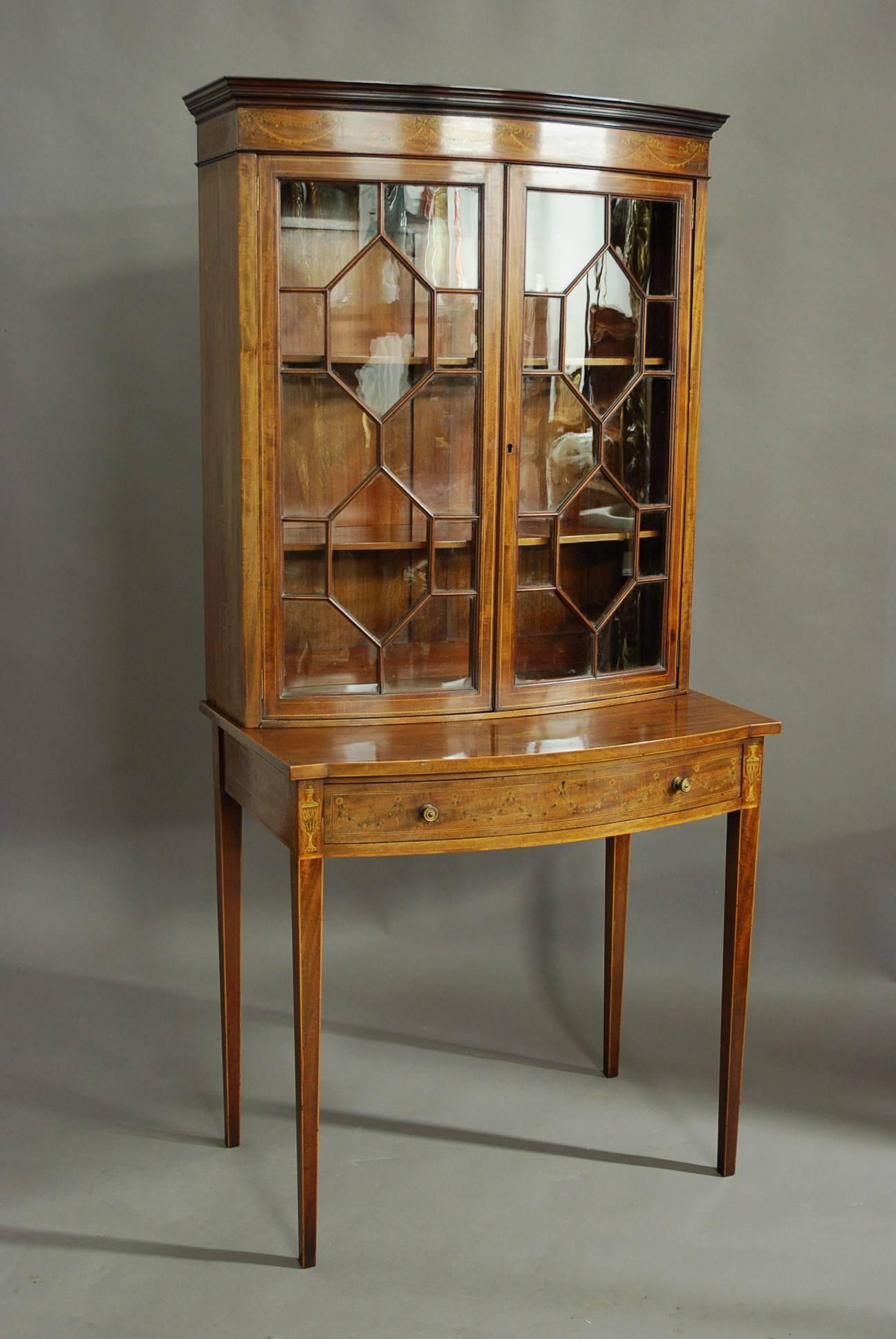 An Edwardian inlaid mahogany bow front glazed display cabinet (or bookcase) in the manner of Edwards & Roberts.

The cabinet consists of a moulding to the top with a frieze below of fine quality inlaid ribbon and swag decoration.  

This leads