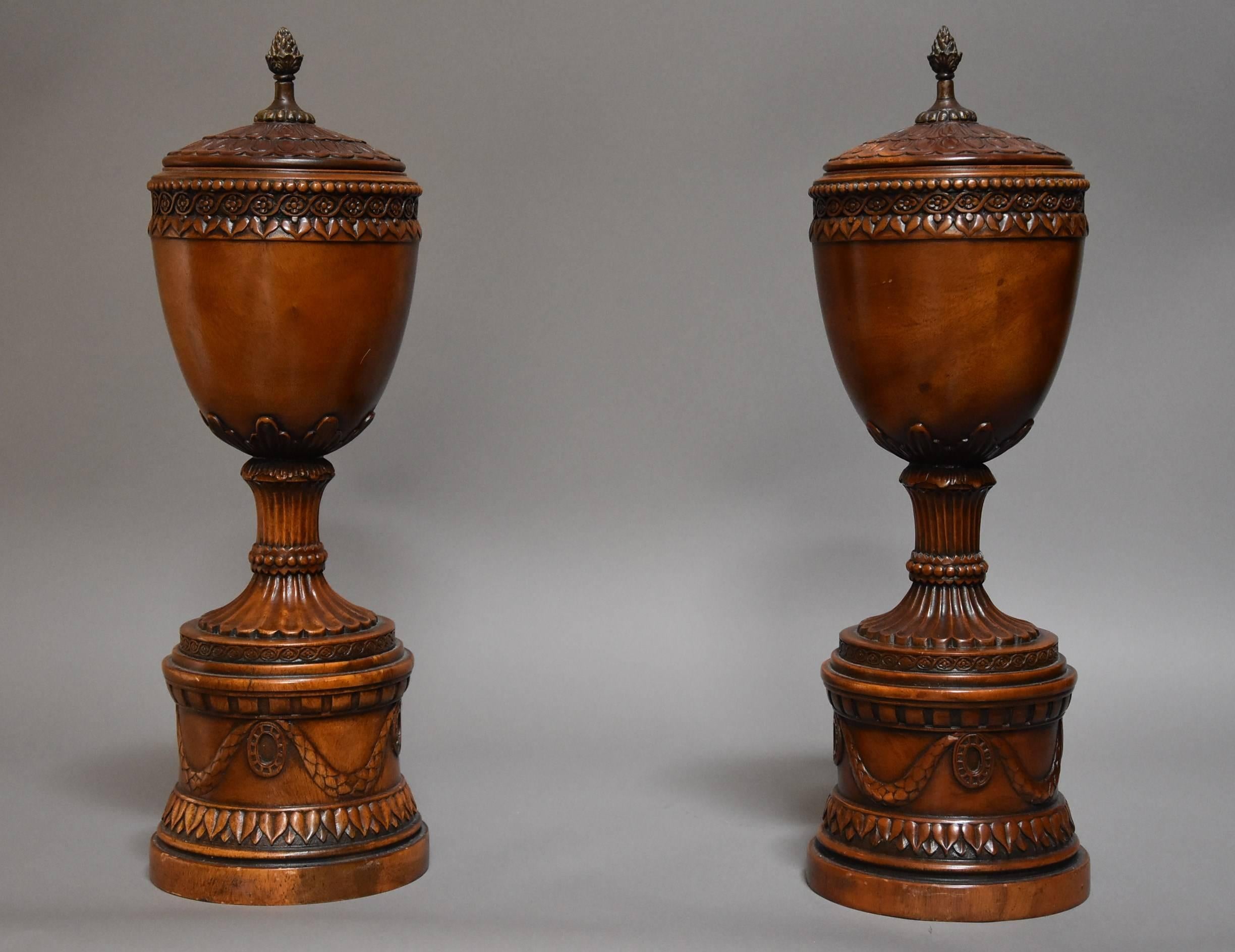 A finely carved pair of early 20th century decorative wooden urns with lids.

This pair of urns each consist of a lid with pineapple finial surrounded by finely carved decoration leading down to a rim with carved ball decoration and entwined