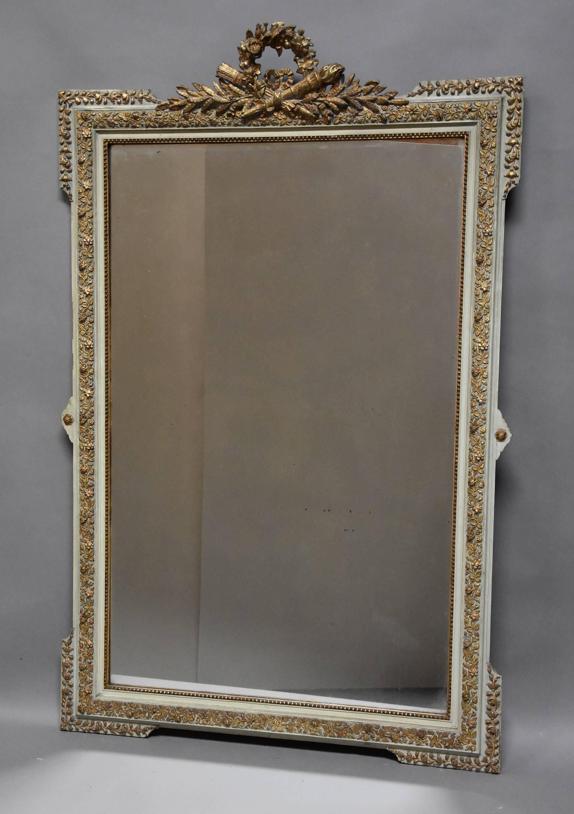 A large late 19th century highly decorative French gilt and painted mirror in the Louis XVI style.

The mirror consists of a floral wreath to the top with ribbon, torch and quiver and arrow decoration with foliage below.

This leads down to the