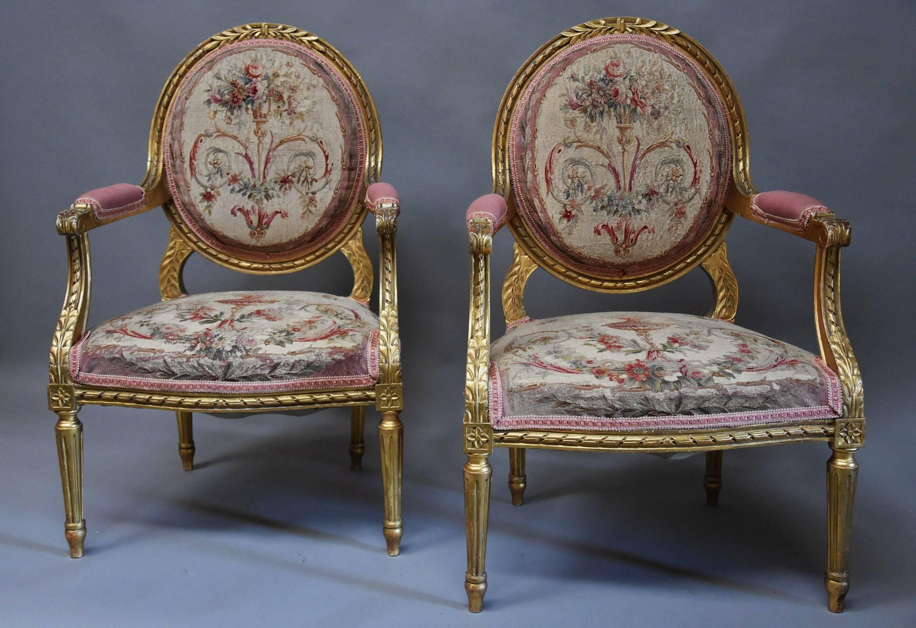 A pair of French late 19th century giltwood open armchairs (or fauteuils) in the Louis XVI style with original Aubusson tapestry covers in pastel tones. 

This pair of armchairs consist of carved oval giltwood backs with foliate decoration to the