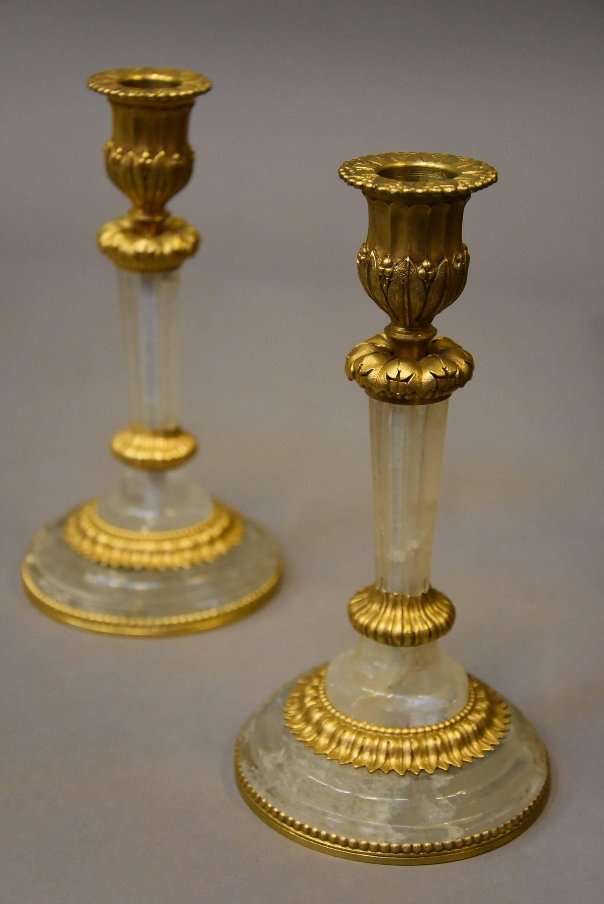 A pair of highly decorative and elegant early 20th century rock crystal and ormolu candlesticks, probably French.

These candlesticks consist of ormolu candle holders with foliate decoration leading down to tapering rock crystal stems with foliate