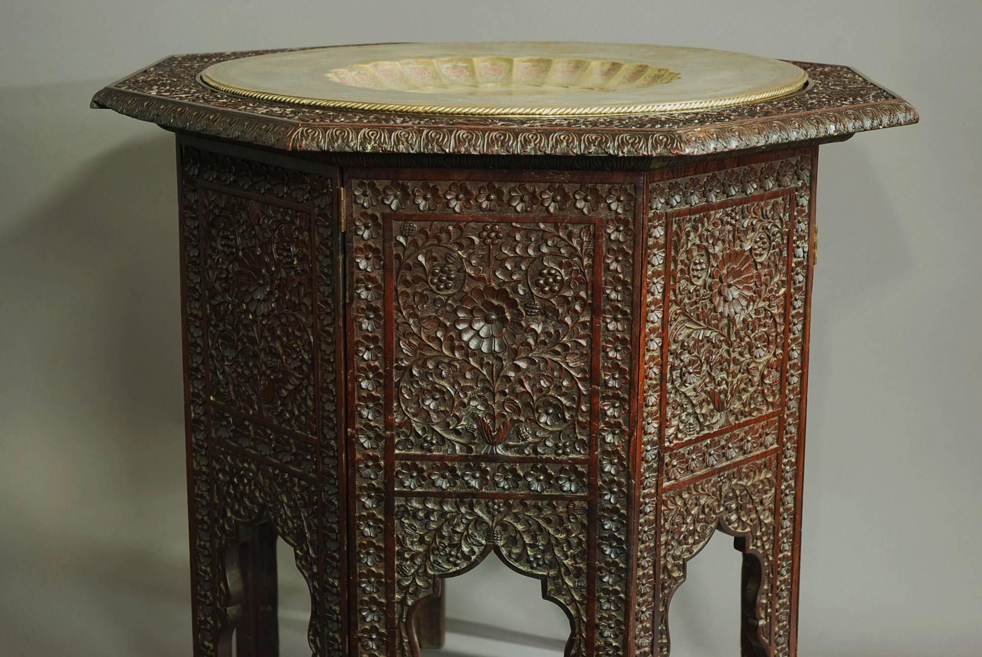 A large late 19th century hardwood highly decorative octagonal Indian table, possibly from the Bombay area.

The top consists of a circular brass inset tray that is supported by the tabletop. The brass tray is engraved and painted with male and