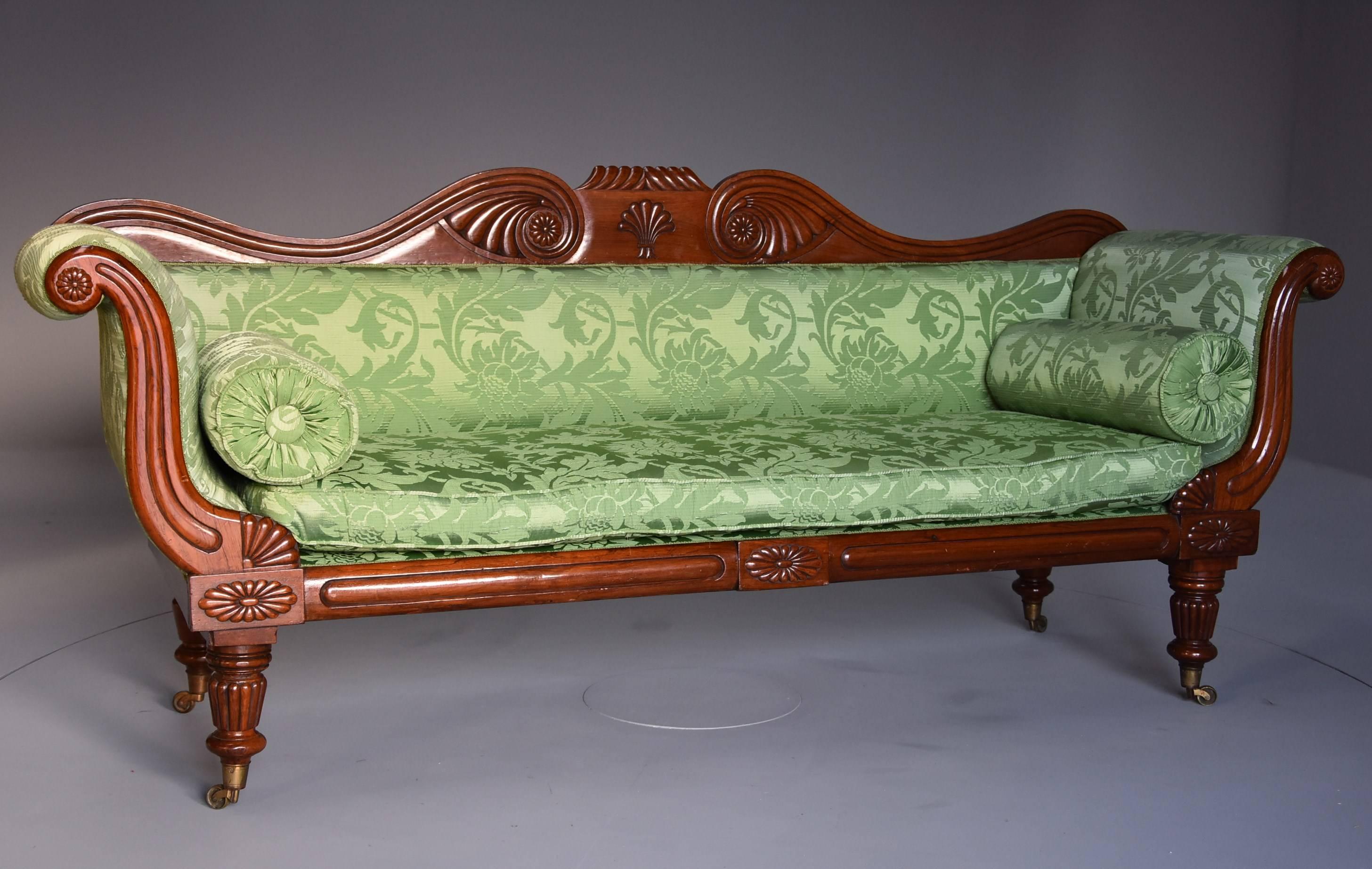 A late Regency scroll end mahogany sofa upholstered in green silk floral and foliate fabric.

This sofa consists of a shaped mahogany back with a central carved gadrooned design with carved shell decoration below with carved scrolling designs to