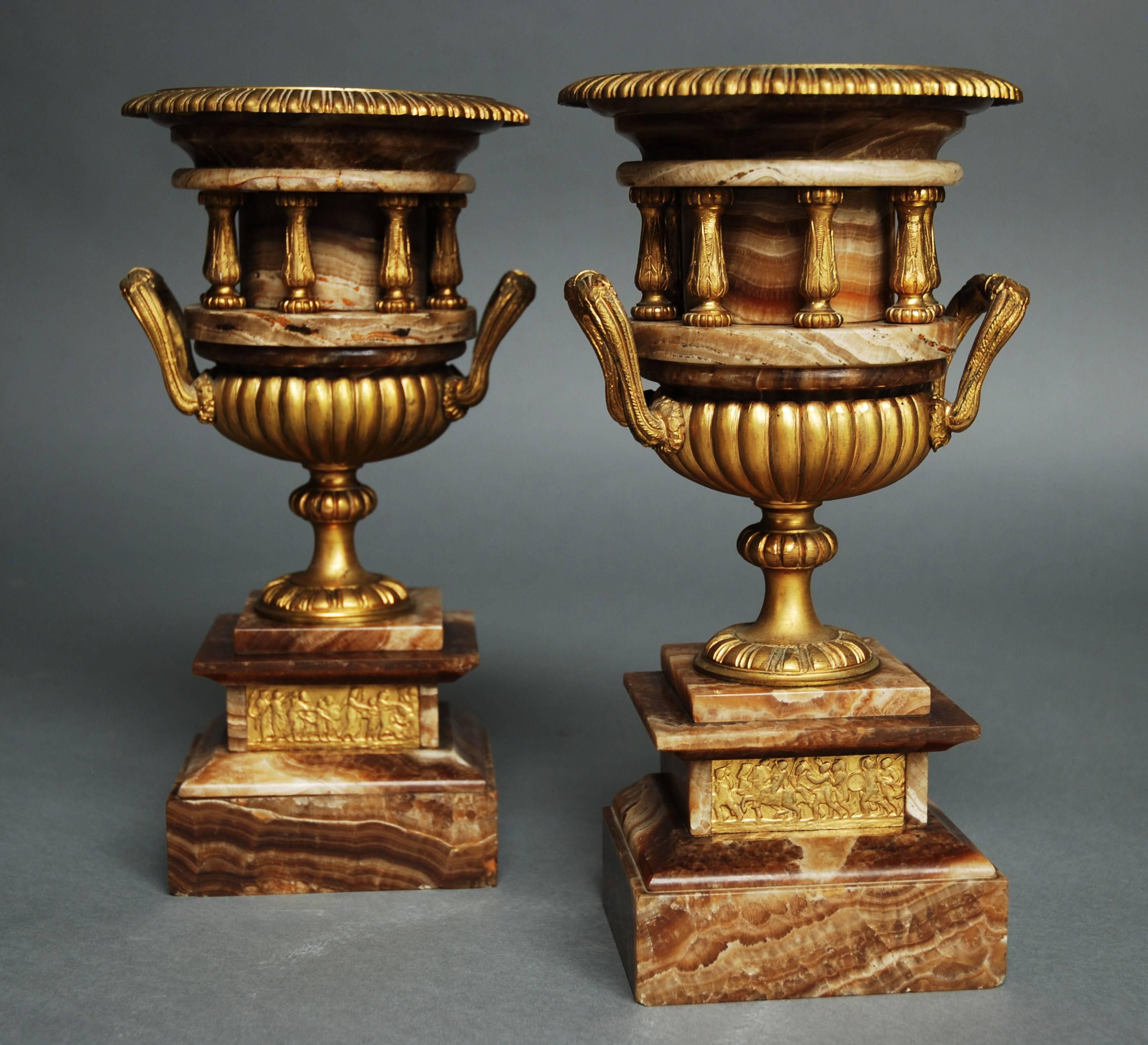 A pair of French highly decorative late 19th century fine quality brown onyx urns with ormolu mounts of small proportion in the Classical style. 

This pair of urns consist of a gilt liner with gadrooned edging leading down to a turned brown onyx