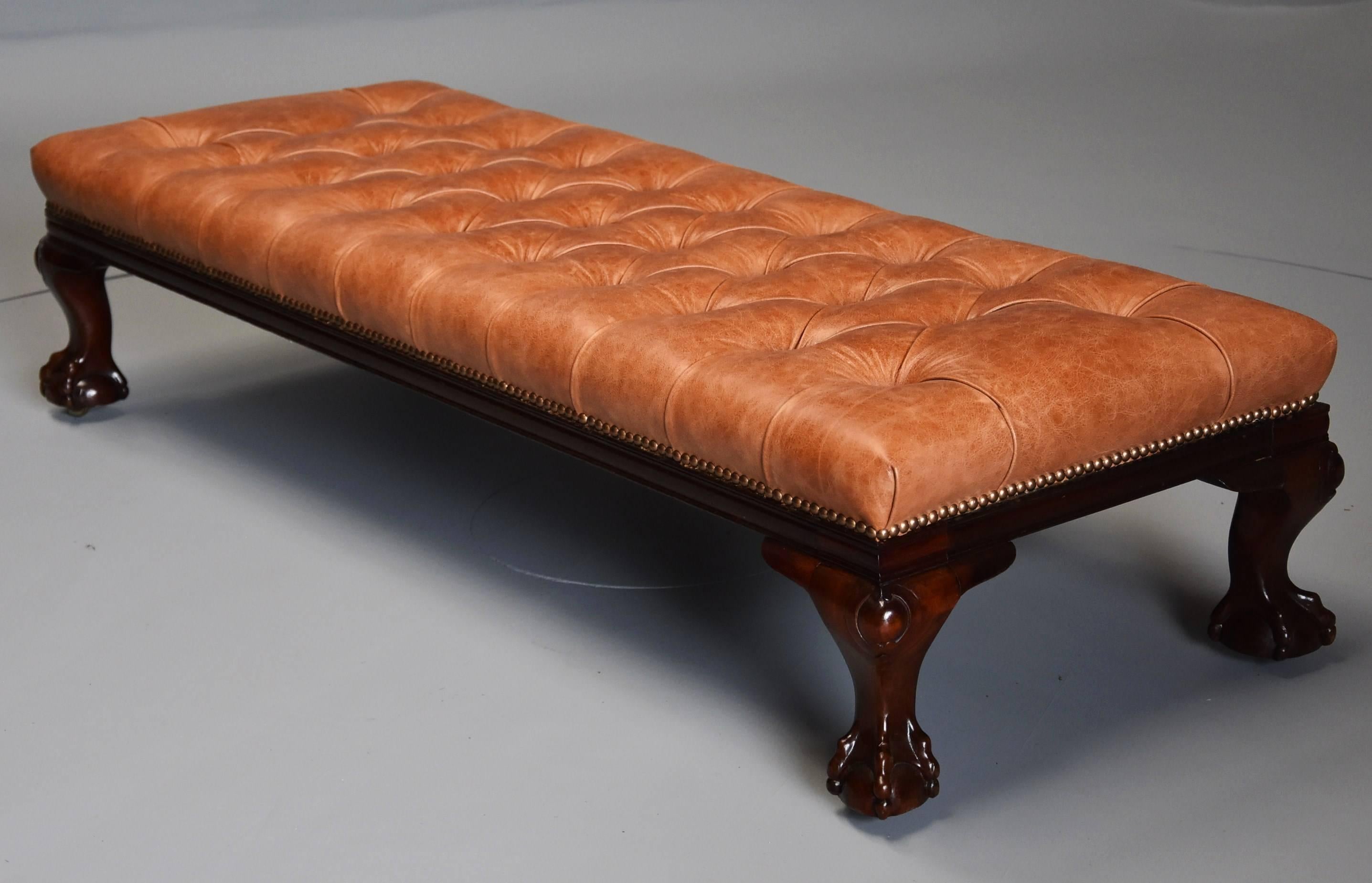 A large mid-19th century deep buttoned tan leather mahogany low stool.

This stool consists of a deep buttoned tan leather top with brass dome-head nails with a moulded edge below standing on four carved cabriole legs leading down to ball and claw