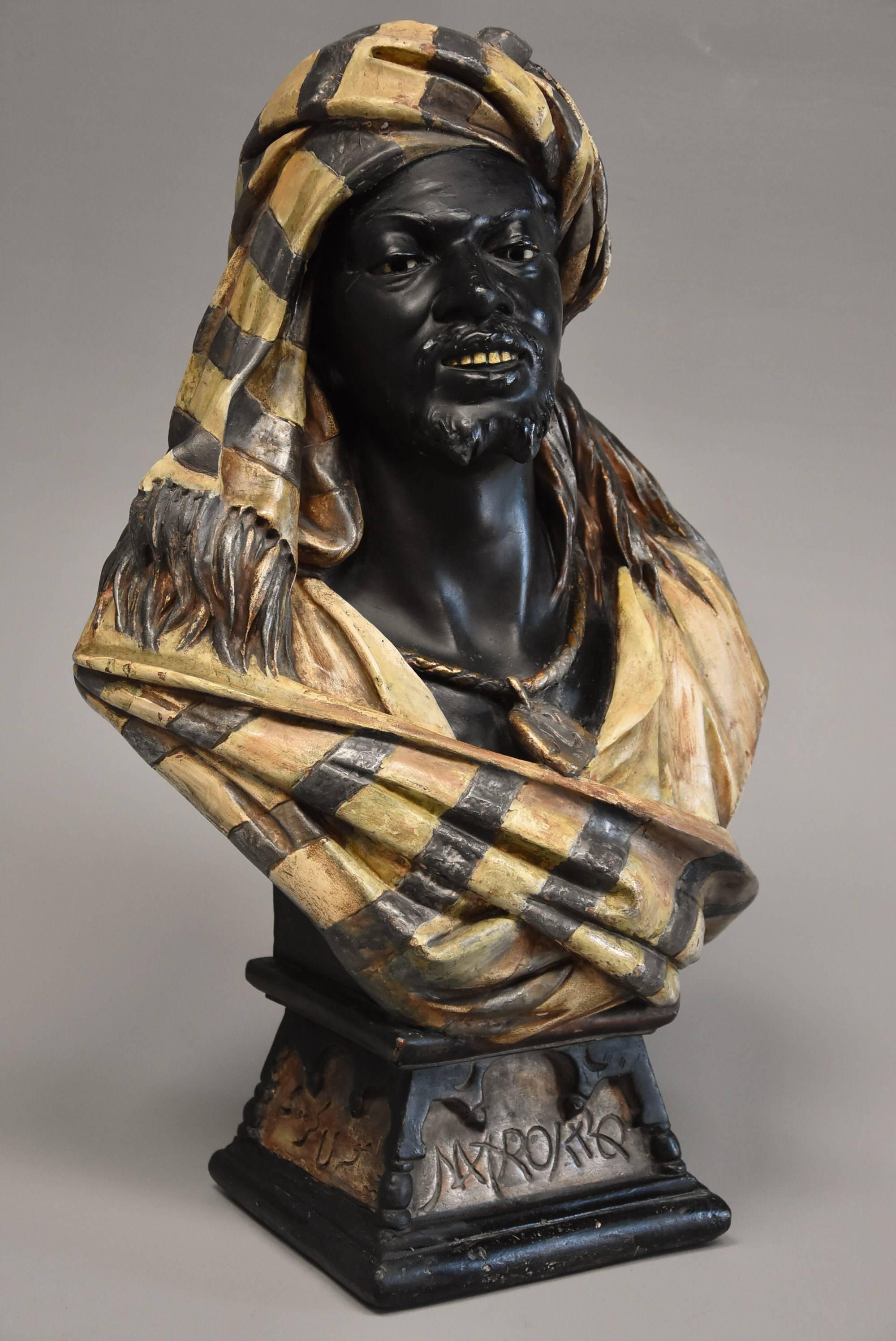 A highly decorative late 19th century lifesize Austrian painted terracotta bust of a Nubian man by Koenig & Lensfeld.

This figure is depicted in exotic traditional dress wearing a shawl, necklace and fez hat.

The figure is supported by a