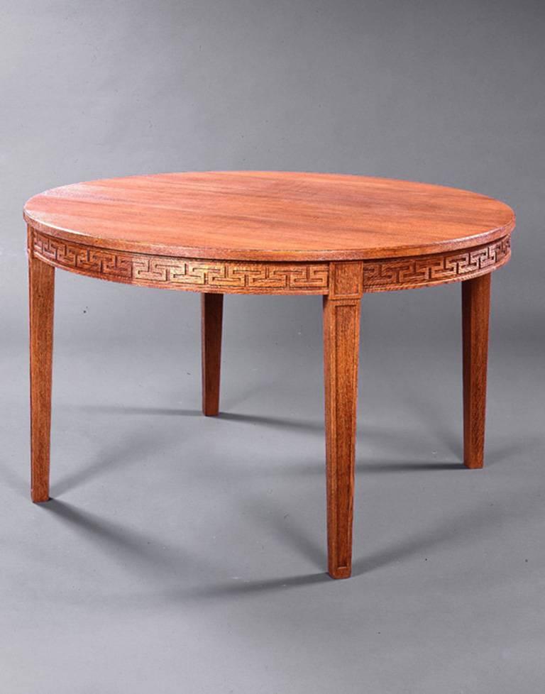 Circular sandblasted oak dining room table with greek wave under the top, raised on four sculpted feet. 
Three extensions. 
Stamped “ j.m. Frank - Chanaux & Cie” and numbered 9394.
Suite of 10 dining room chairs with open back, raised on four