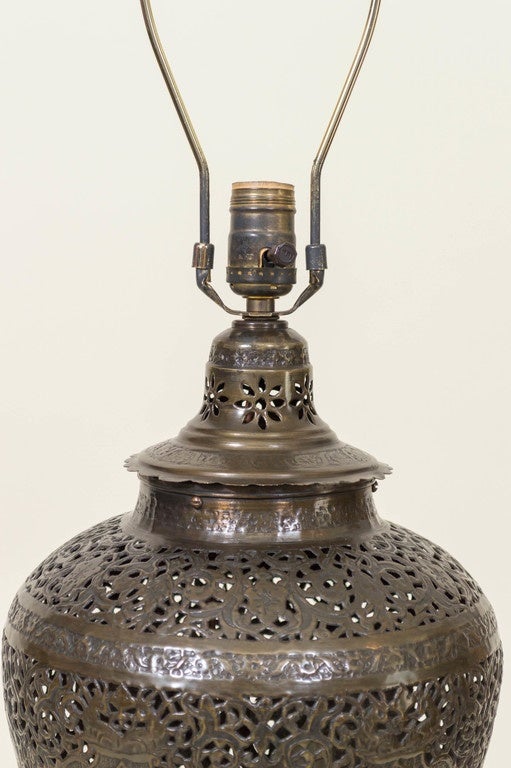 Exotic Persian brass vessel lamp. Reticulated, pierced and engraved design with distinguished portraits of men in armour surrounding the sides. Custom turned dark wood base with heavy weight added to stabilize and ground the delicate lace like