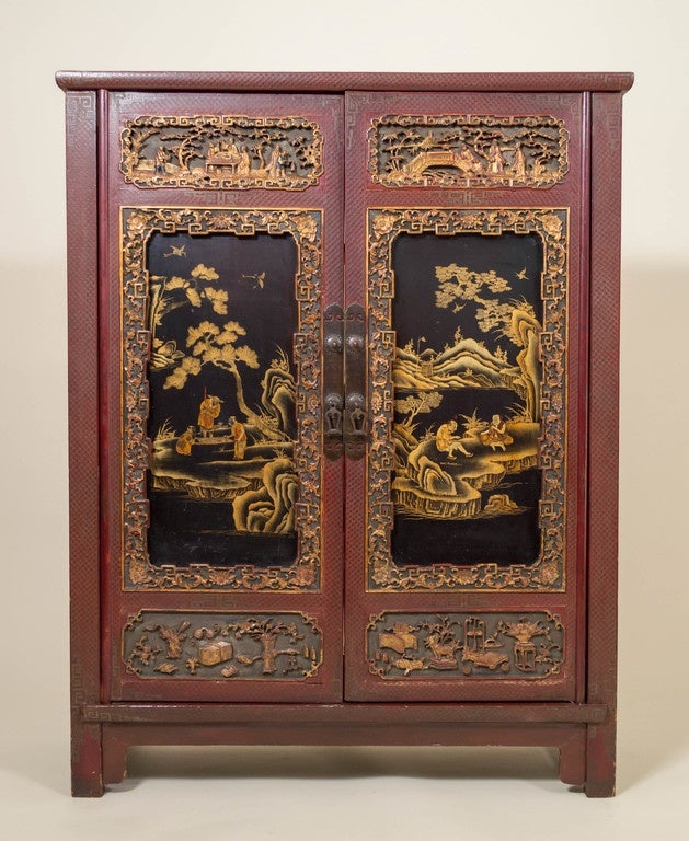 Chinese lacquer, carved and gilt decorated cabinet. Gold gilt decorates the body of the dynamic red cabinet, deep relief carved panel insets and black lacquer central panels with finely drawn men in landscape settings. The top and sides decorated