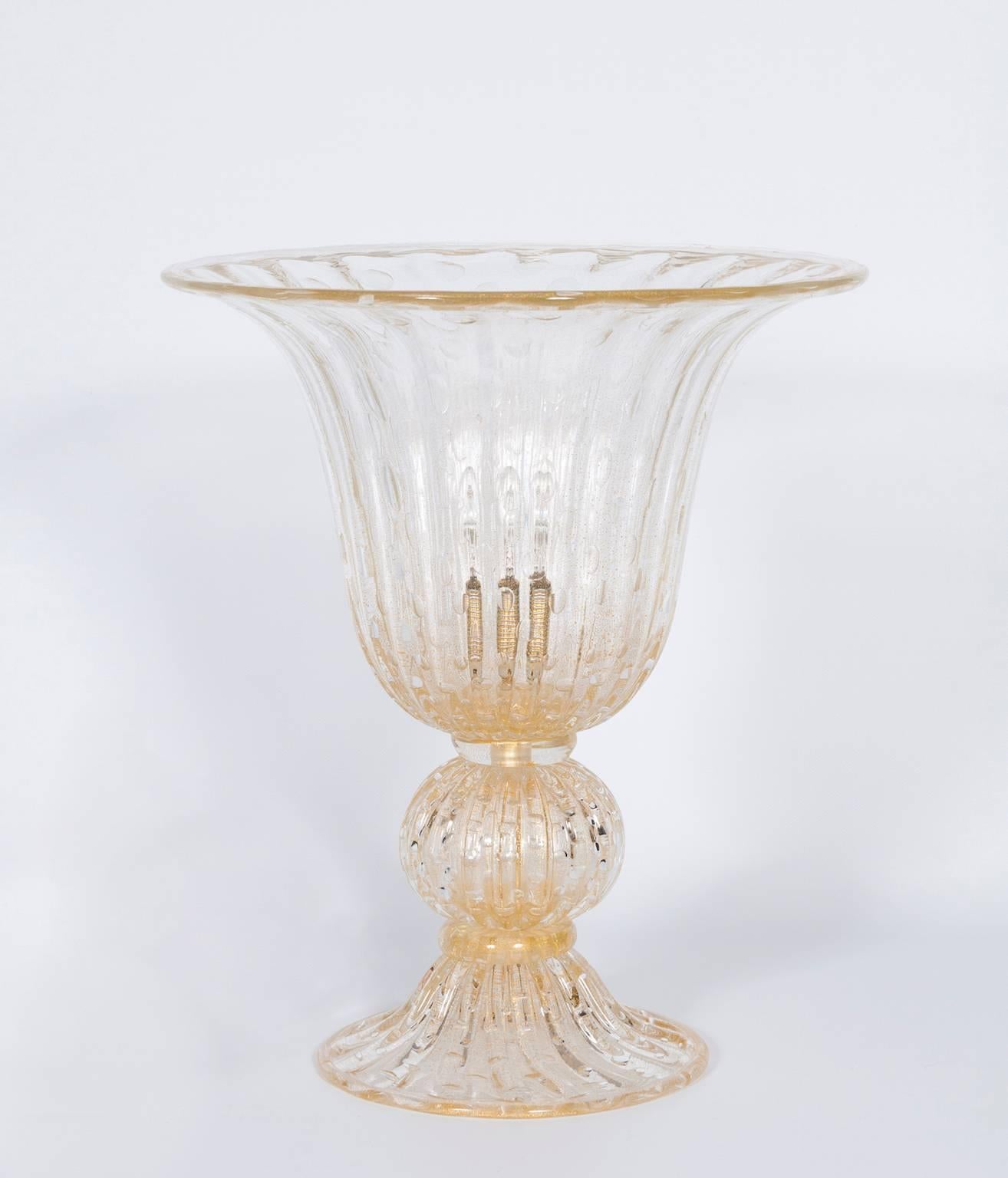 Imposante handgefertigte Murano-Glas-Tischlampe mit versenkten Blasen.
Diese moderne Tischleuchte, die vollständig aus exquisitem Murano-Glas in einem satten Goldton gefertigt ist, verkörpert italienische Kunstfertigkeit. Das bezaubernde Design mit