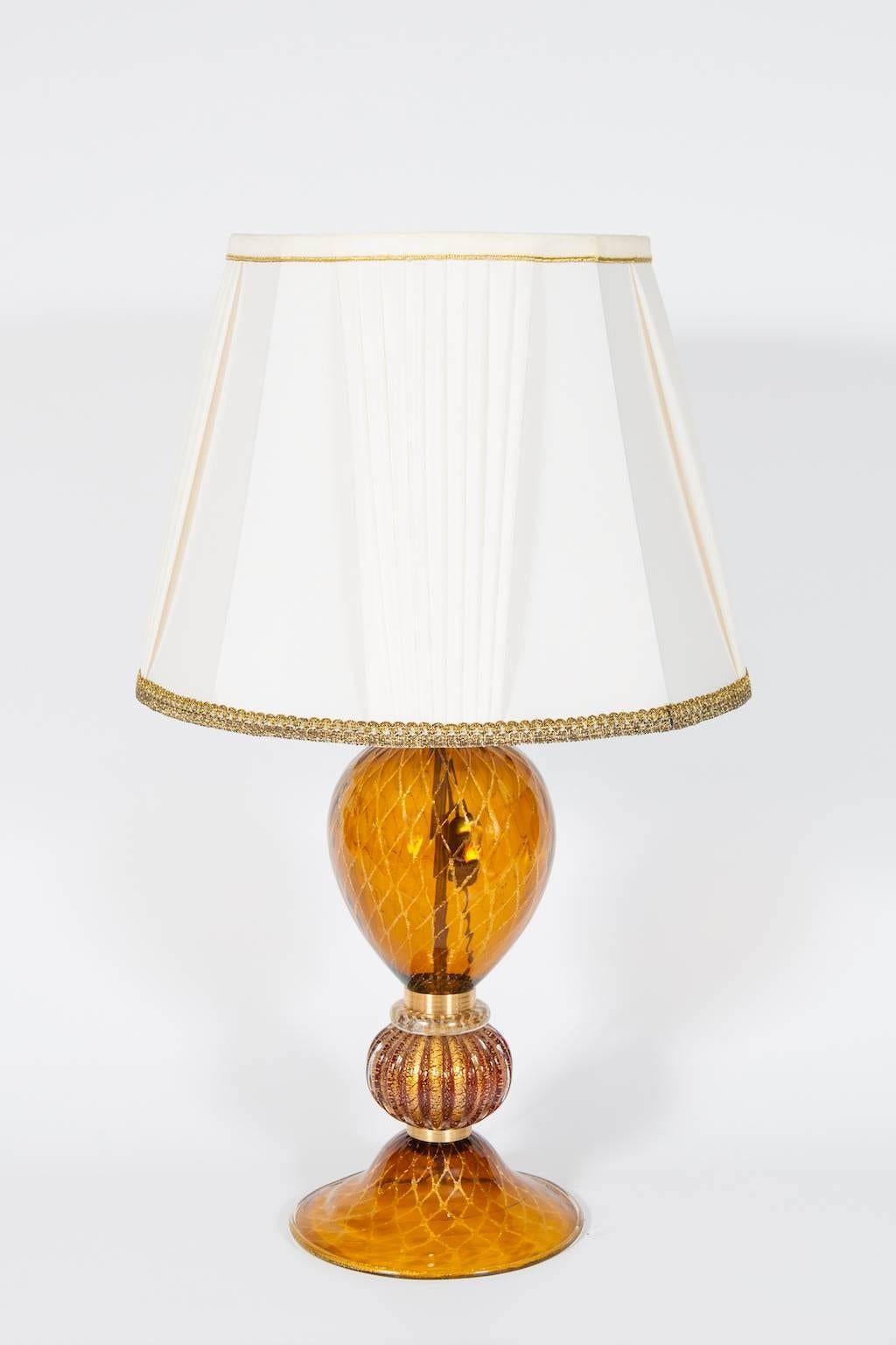 Élégante et unique lampe de table vénitienne italienne,  Verre soufflé de Murano, ambre et or 24 carats, années 1980.
Ce portrait est composé d'un socle et d'un corps principal en verre ambré avec des bandes d'or 24 carats en forme de nid d'abeille.