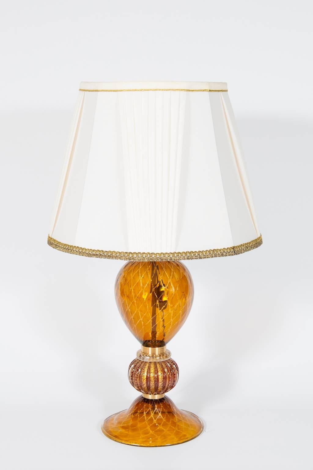 Elegante e unica lampada da tavolo veneziana italiana,  Vetro soffiato di Murano, ambra e oro a 24 carati, anni '80.
Questo ritratto è composto da un basamento e da un corpo principale in vetro ambrato con strisce in oro 24 carati a forma di nido