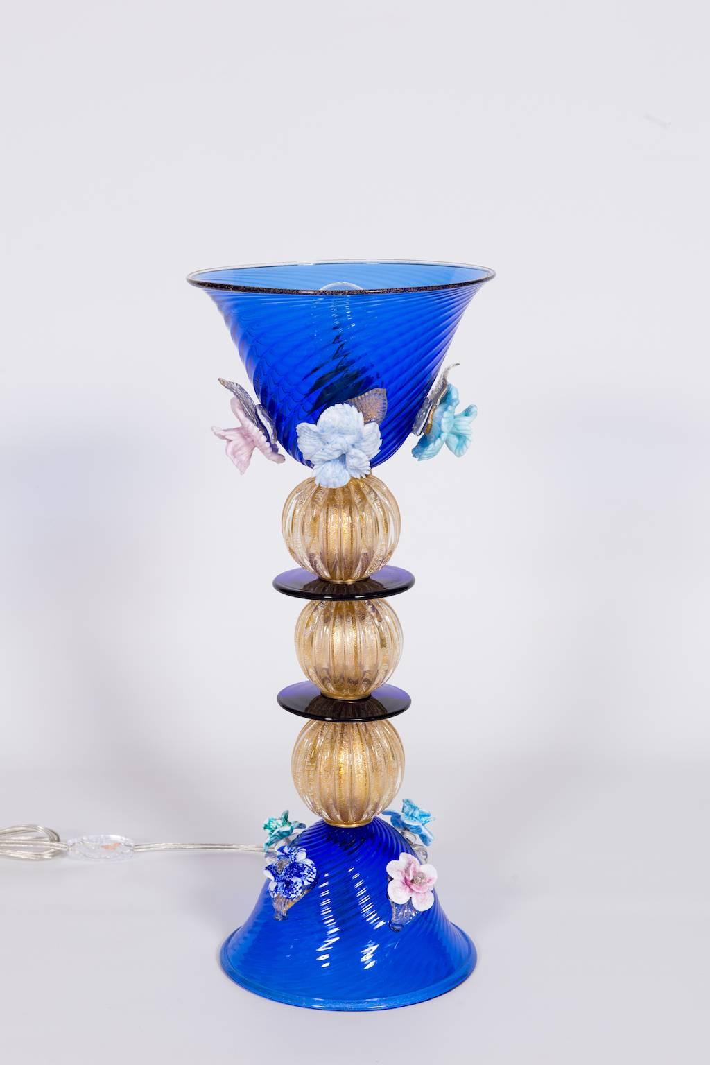 Italian table lamp in blue and 24-karat gold and multicolor Murano glass, composed by a blue base with four flowers, by above three 24-karat gold spheres divided by circular blue disks, with above a cup with four flowers , with inside a light,