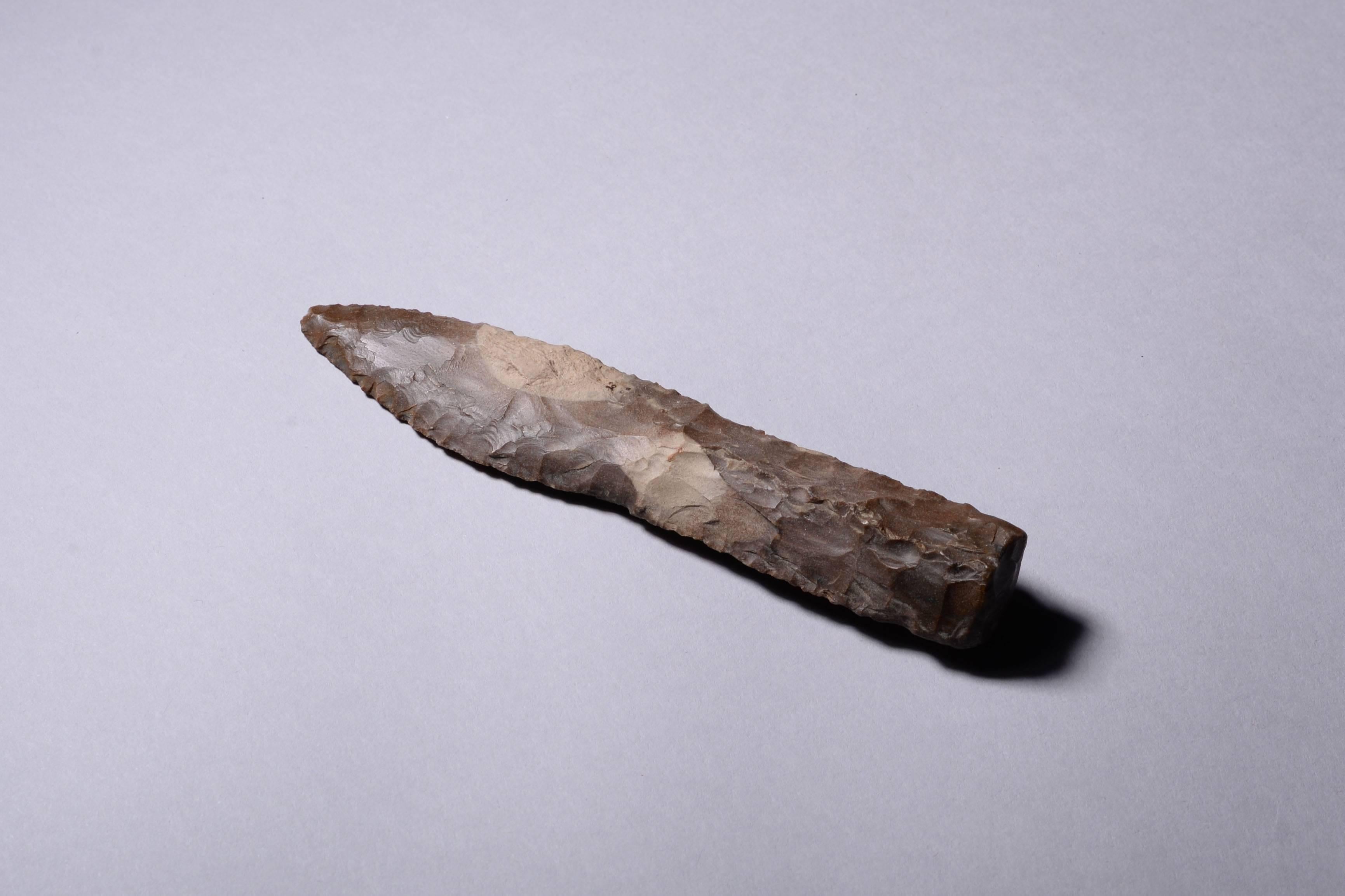A Neolithic flint “type III” dagger, from Scandinavia, dating to 1900-1700 BC. Flint daggers such as this represent the pinnacle of prehistoric flint working. Pressure flaked from a piece of chocolate-grey colored flint, the blade is leaf shaped,