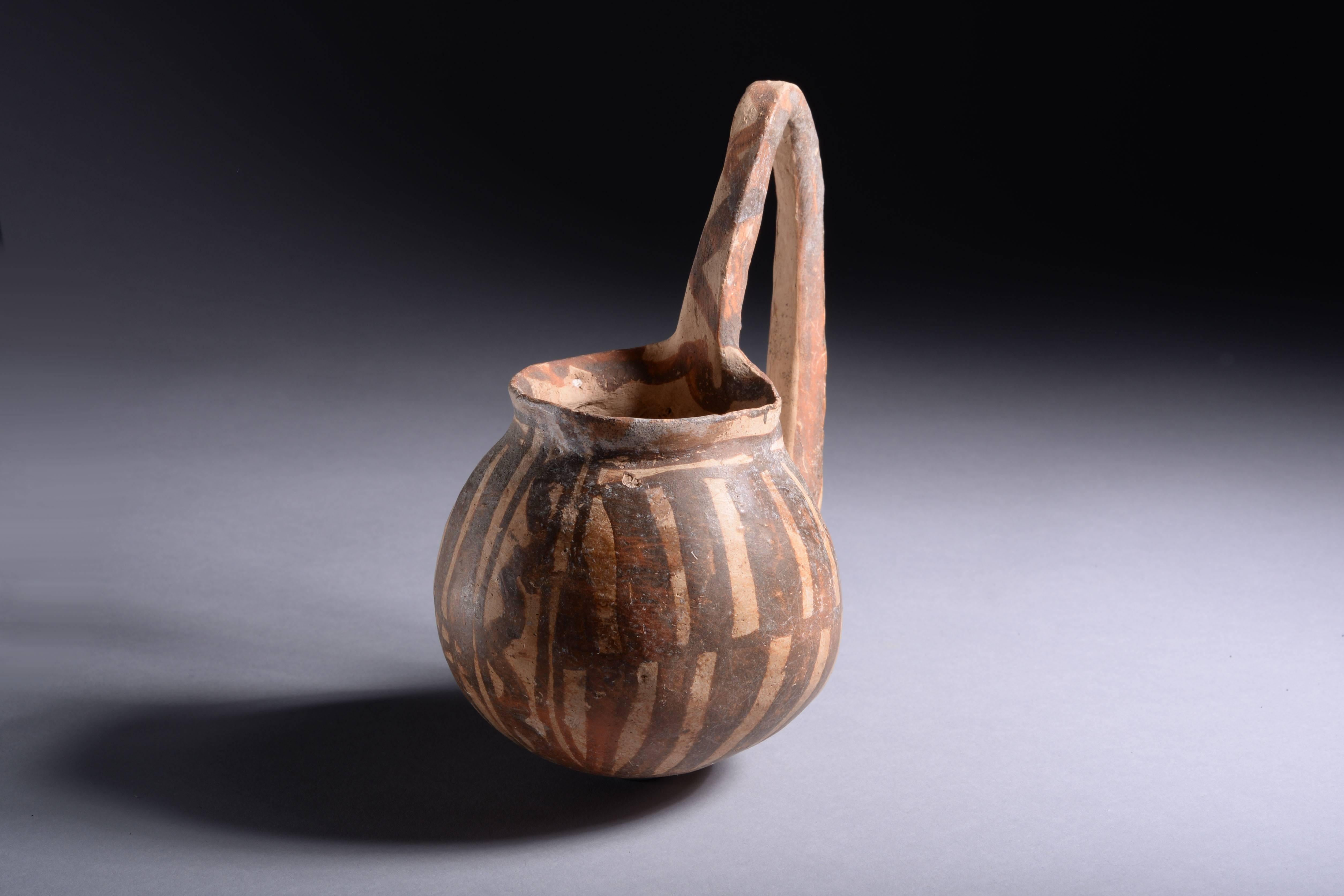 An ancient Cypriot middle Bronze Age white painted ware dipper cup, dating to around 1900 BC.

The deep bowl with everted rim and rounded base, adorned with a tall ‘wishbone’ handle. The body decorated with geometric patterns painted in mauve on