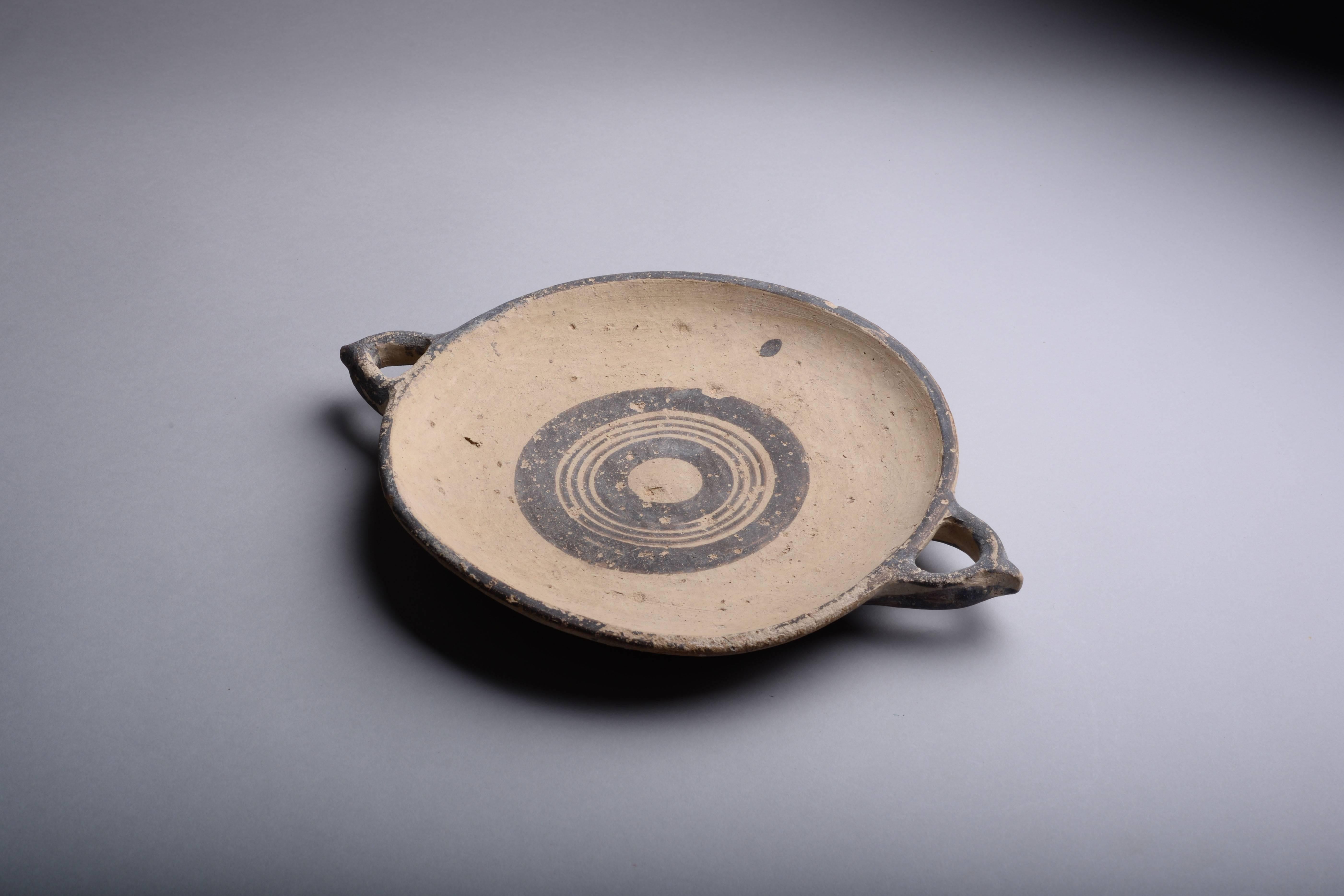 An exceptionally rare Cypro-Geometric plate, decorated profusely with a hunting scene, dating to circa 1050-600 BC.

The plate has shallow sides and ring base. There are two opposed horizontal loop handles which have simple nipples at their