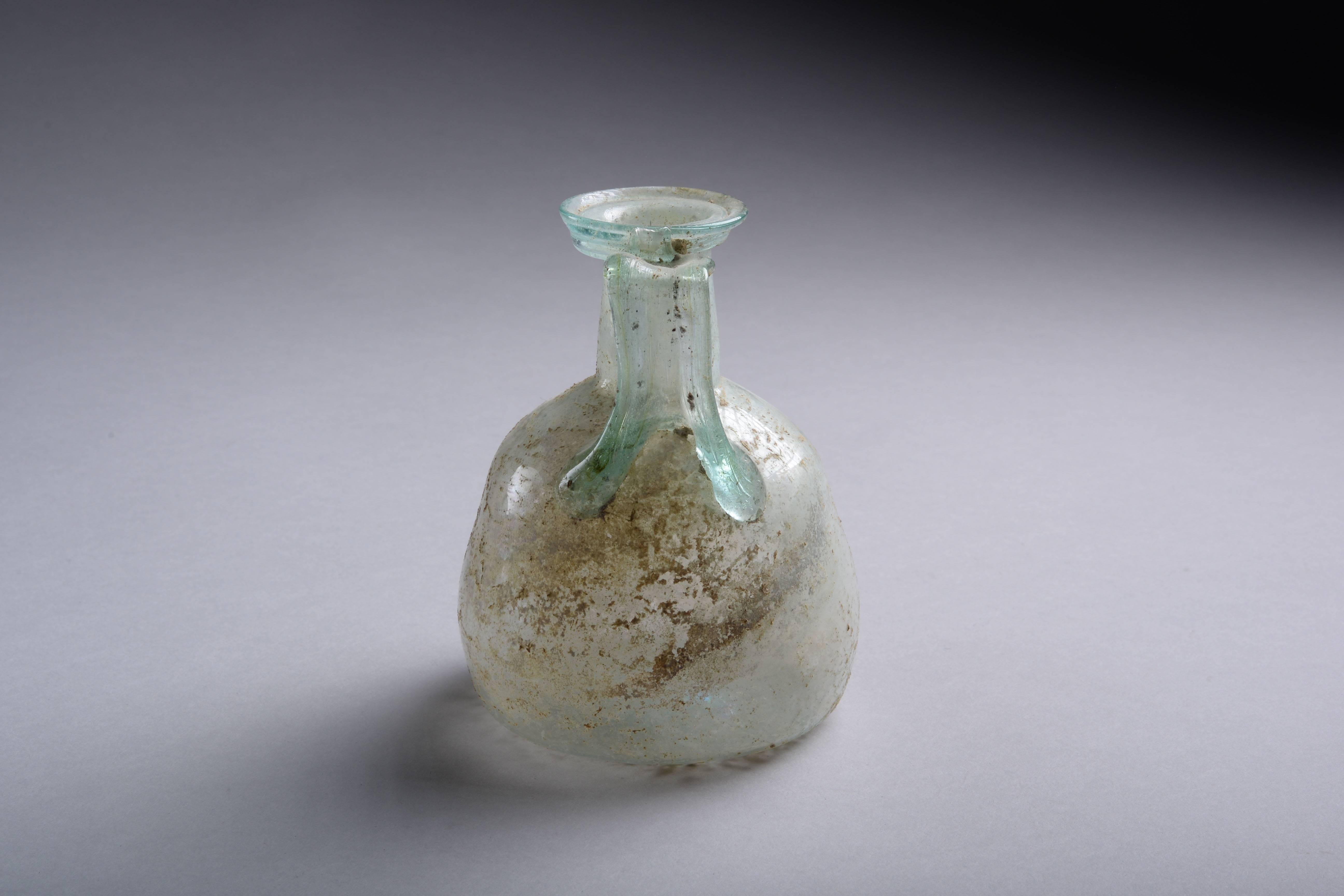 A fine and beautifully preserved Roman glass jug, dating to the first-second century AD.

Free blown, with rounded body, curved shoulders, cylindrical neck and round disc shaped mouth, with a separately applied trail handle, the base with remnants