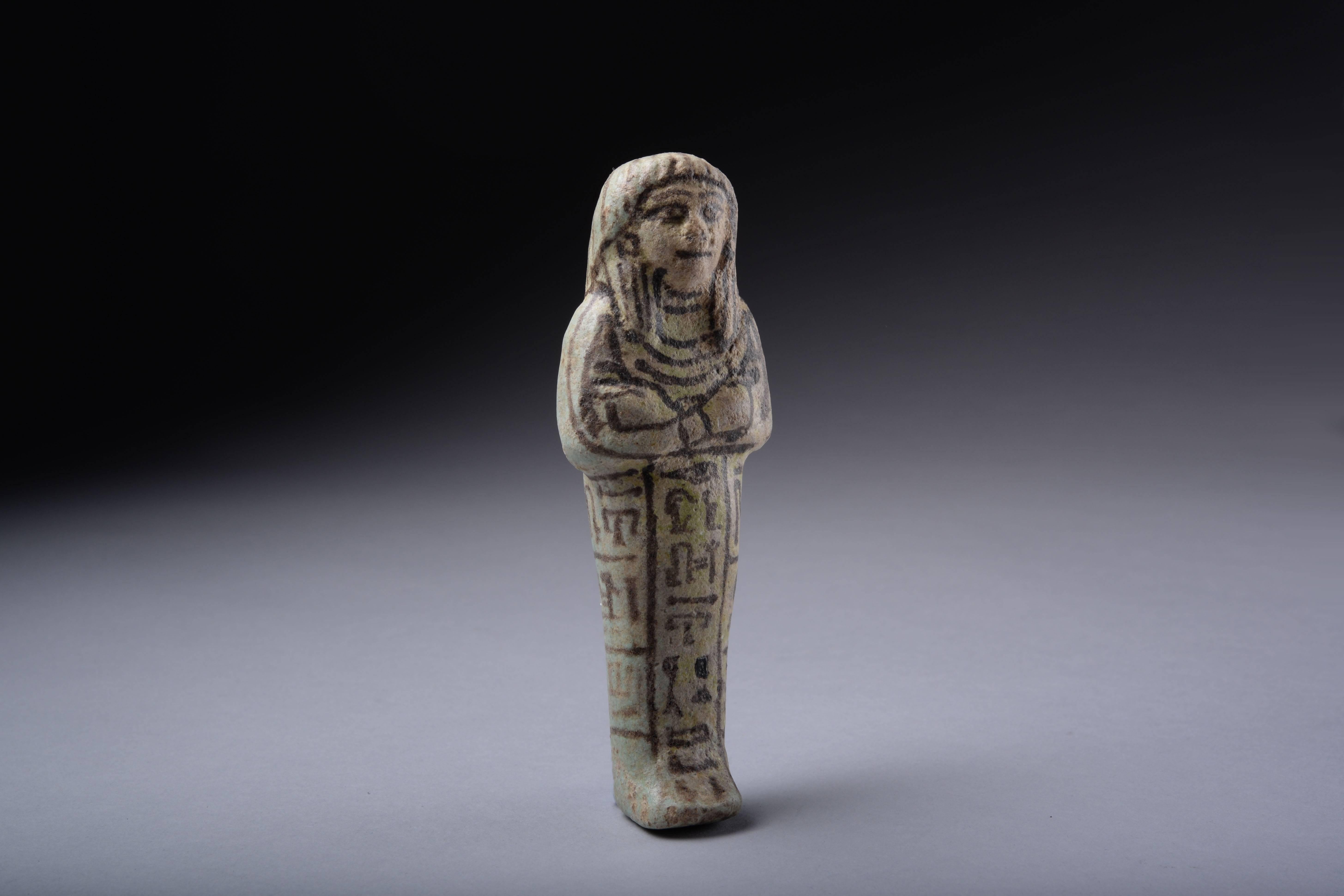 A finely modeled, and well preserved ancient Egyptian faience shabti for May, Scribe of Ptah, dating to the 19th-20th dynasty, circa 1291-1064 BC.

The figure is depicted mummiform, with arms crossed holding two hoes, wearing tripartite wig, a