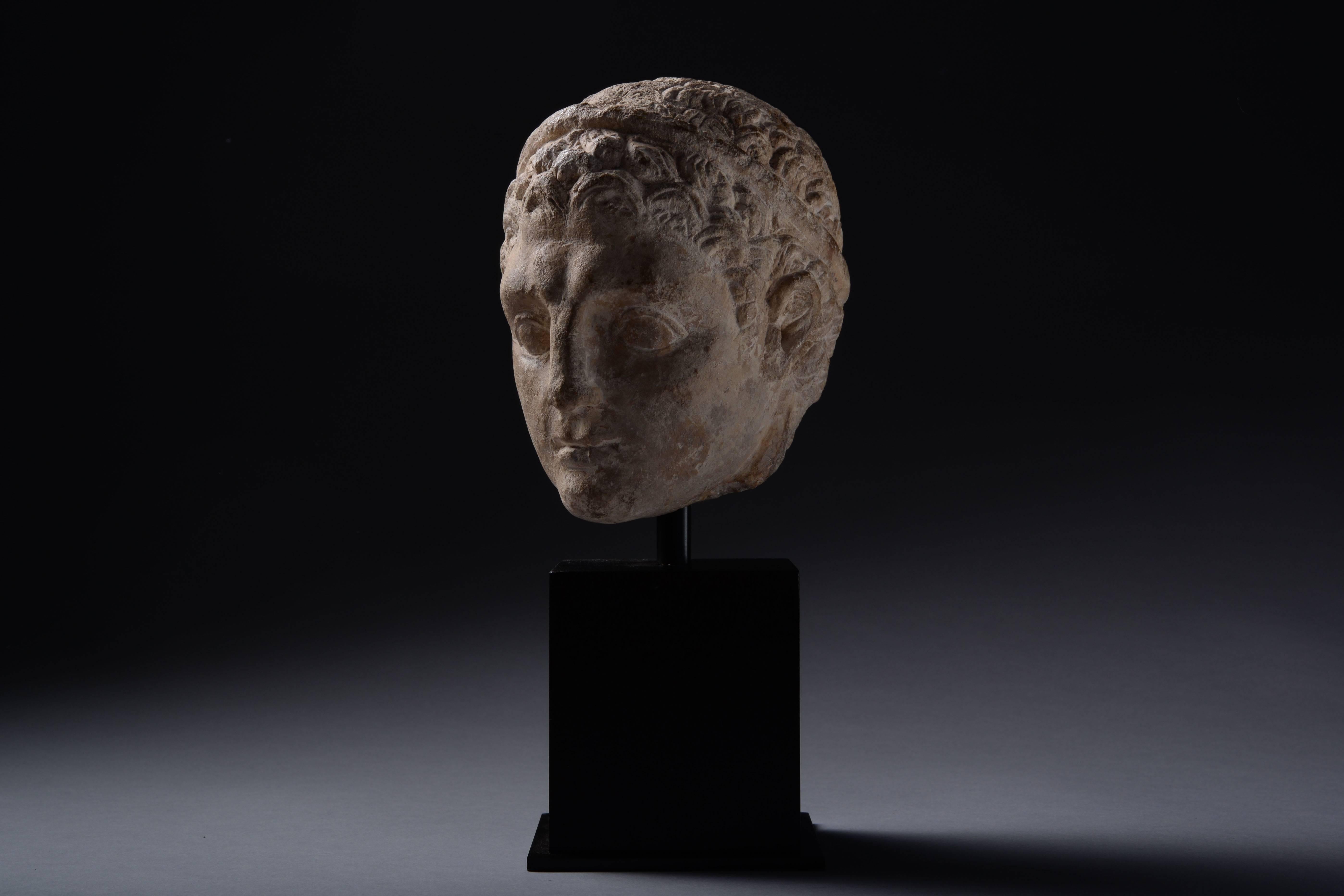 A rare and well provenanced ancient Cypriot limestone head of a Votary, dating to 350 BC.

The youthful figure is shown with diadem, curled hair and powerful features. The style is reminiscent of Greek Hellenistic sculpture, but it is carved in