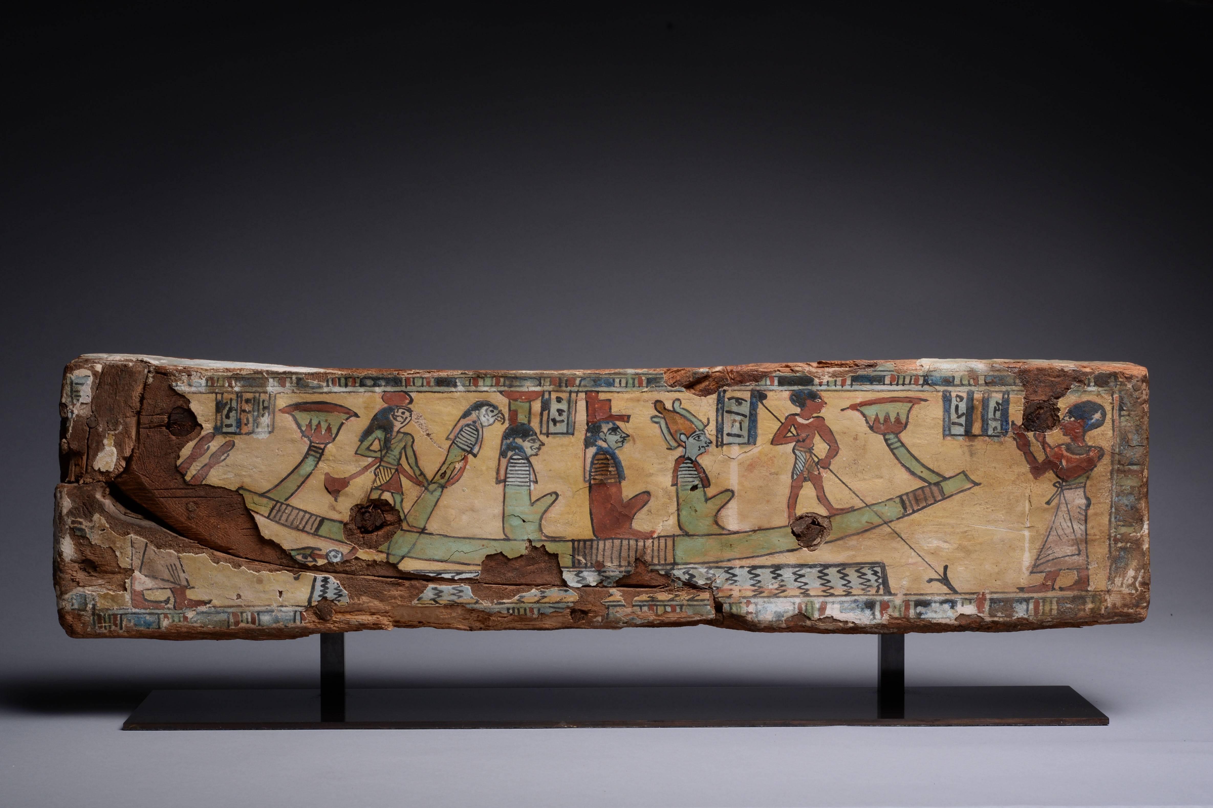 A vibrant ancient Egyptian painted wood panel. Depicting a well known scene from the Book of the Dead. Dating to the Ptolemaic period, circa 100 BC.

Showing the deceased standing at the helm of the solar boat, sailing through the dark and