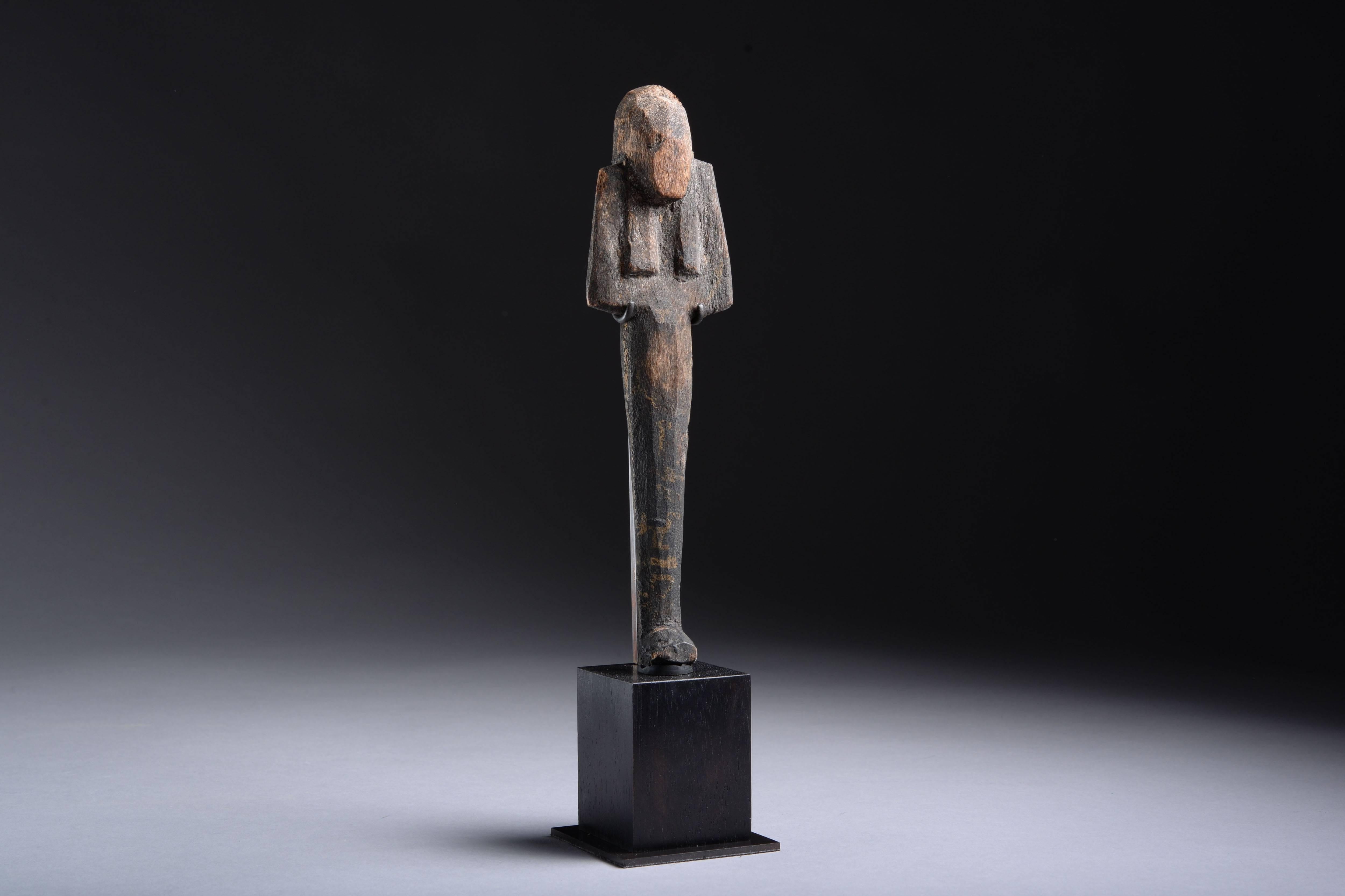 A well provenanced and striking ancient Egyptian wooden shabti, dating to the New Kingdom, Ramesside Period, 19th-20th Dynasty, circa 1295-1070 BC.

The figure is depicted mummiform, with long slender body, tripartite wig and folded arms. A