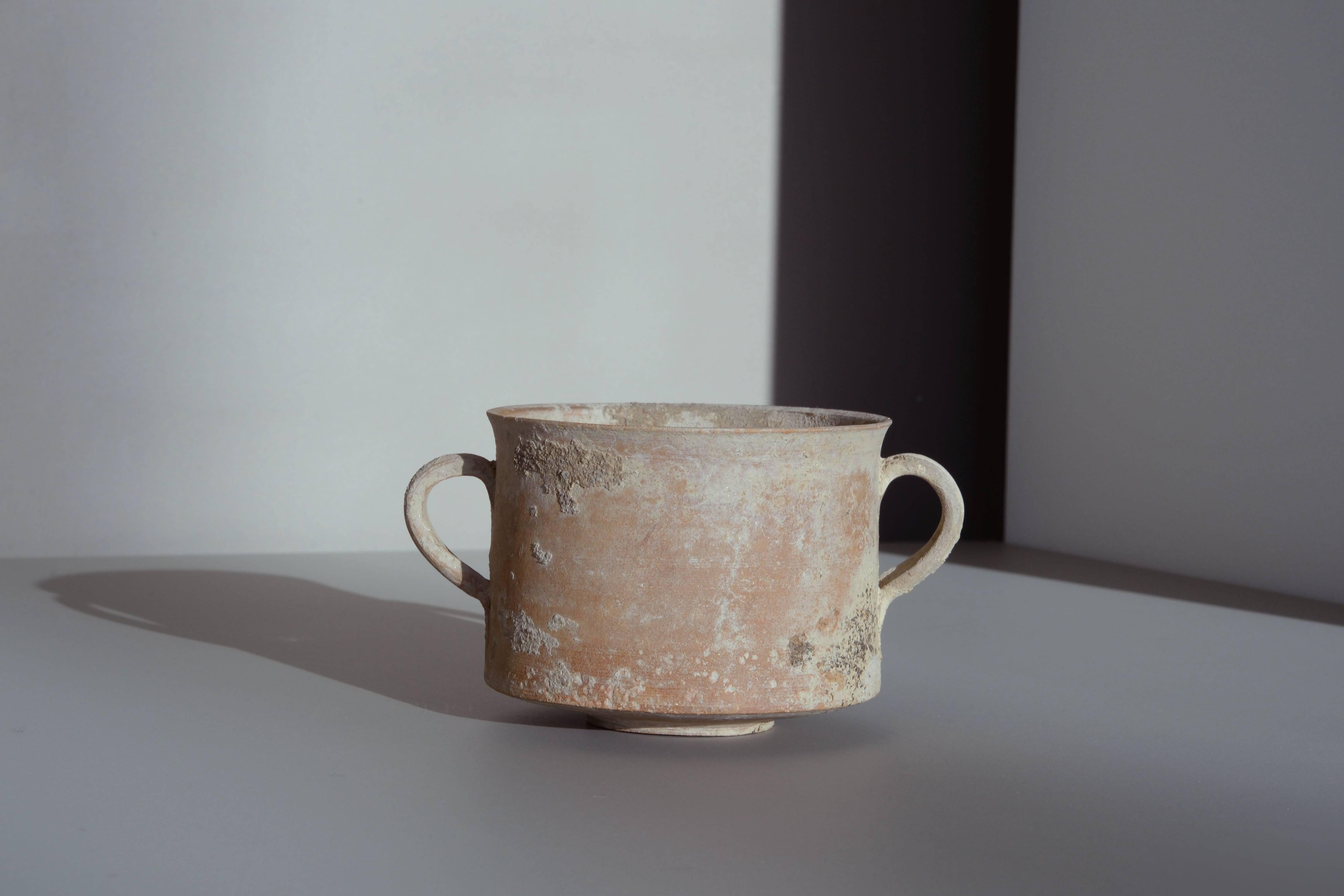 An ancient Roman pottery skyphos, dating to the 1st century AD.

Of particularly elegant form, finely potted, with round foot and flat base, straight walled sides and subtly turned out rim, two ear shaped handles positioned bilaterally.

A