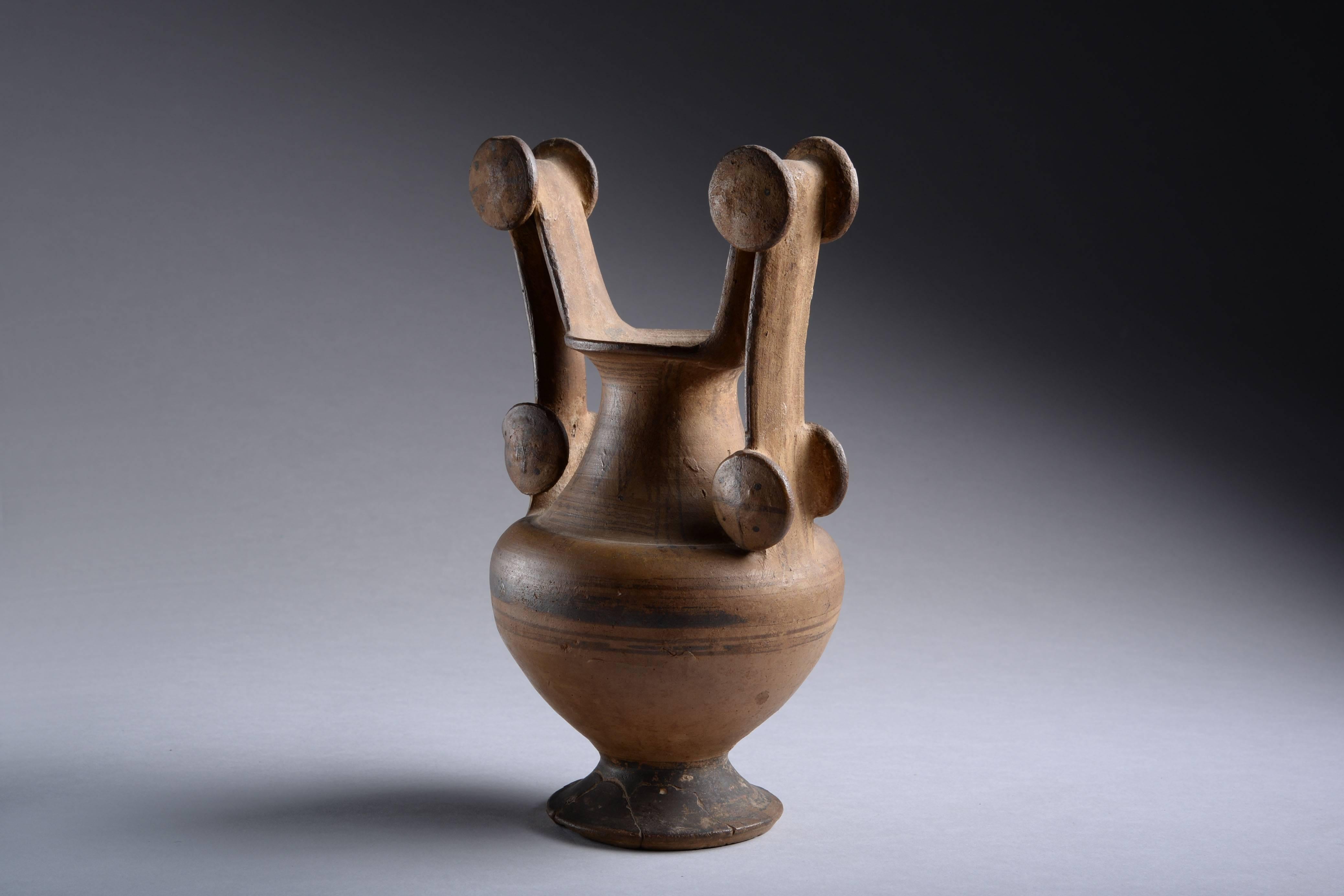 An ancient Apulian Messapian ware trozella, dating to the 4th century BC.

Standing on a splayed foot, with rounded body, tapered, cylindrical neck and flaring rim. The wonderfully elaborate, tall, angular handles decorated with applied rosettes.