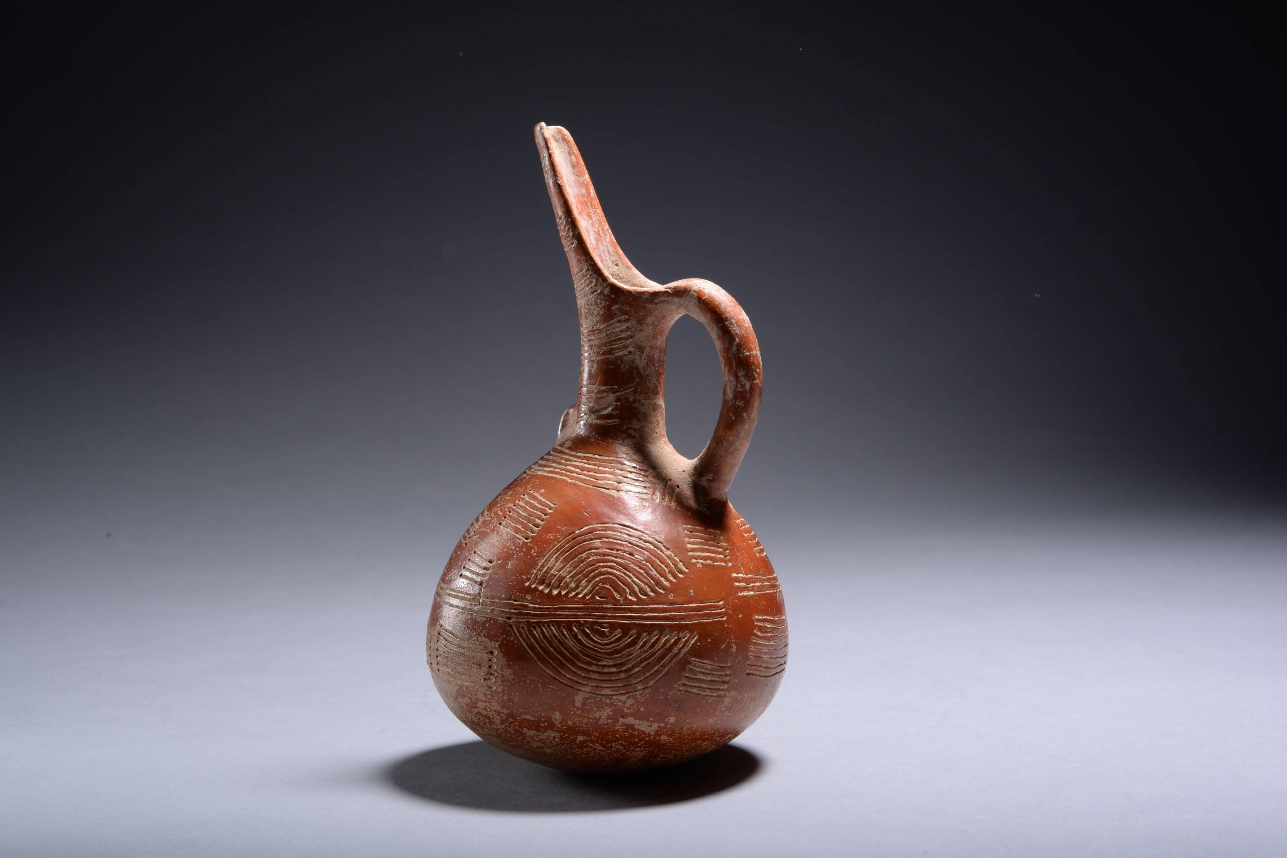 An incised red polished ware jug from Cyprus, dating to the early Bronze Age, circa 2300-2000 BC. 

With rounded, globular body and cylindrical neck, cutaway-beak spout and a loop handle, a small boss at the base of the neck. Decorated throughout
