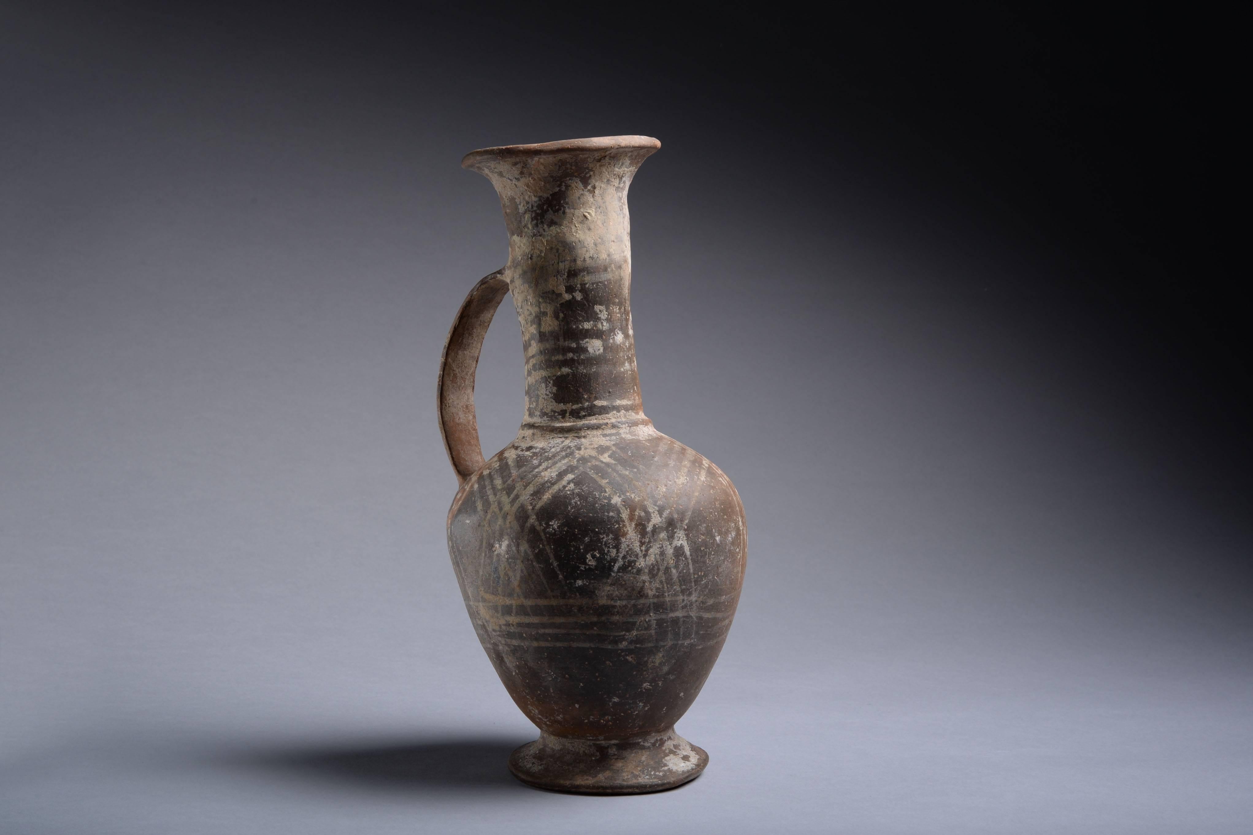 A base ring ware jug from Cyprus, dating to the Late Bronze Age, circa 1550-1200 BC.

With ring base, plump body, cylindrical neck, rimmed mouth and strap handle. Potted from orange clay and covered with a mottled orange and grey slip and