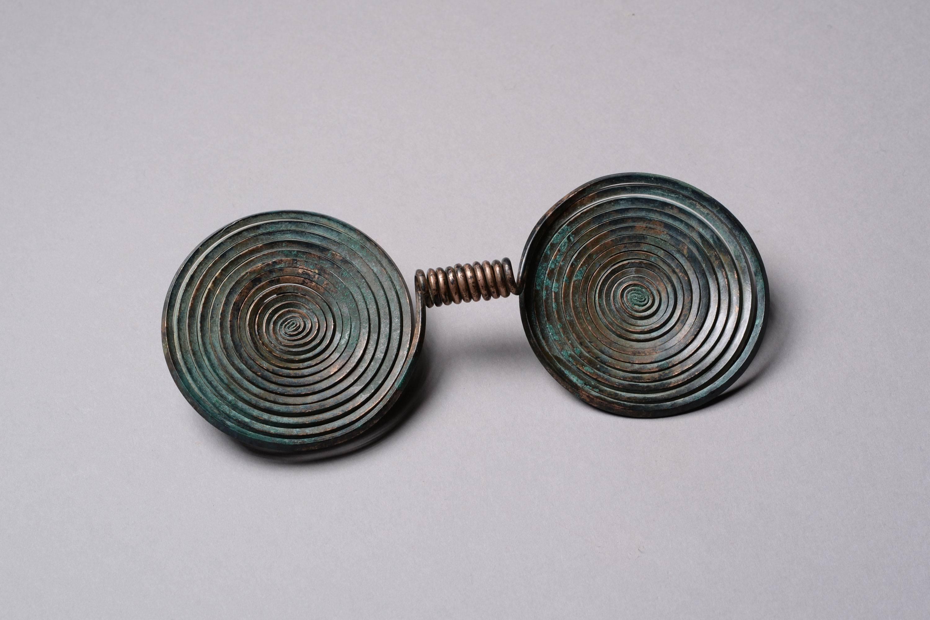 A stunning central European Bronze Age brooch, dating to around 1000 BC.

The piece has been expertly cast into two conjoined spirals of wired disc, meeting in a tight coiled band at the center. The late Bronze Age in Europe saw a flourishing of