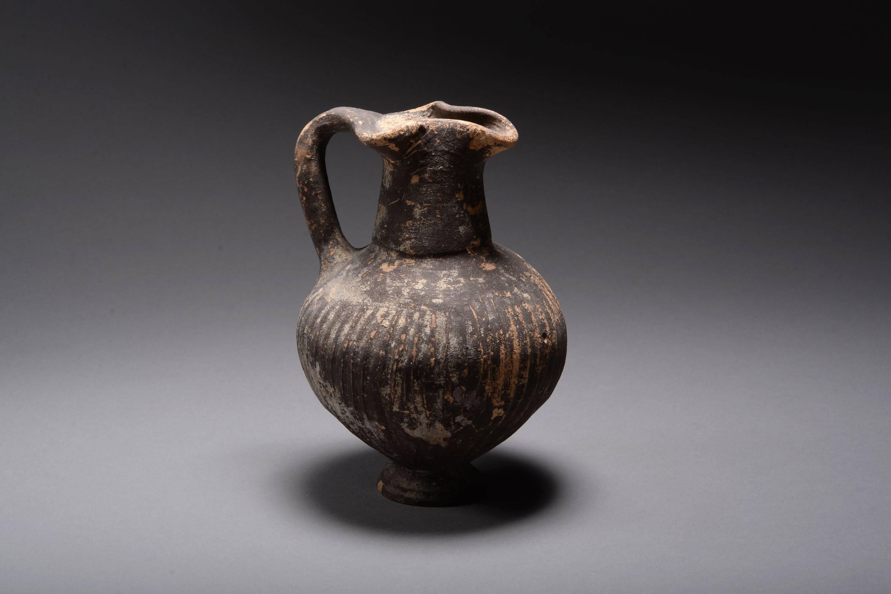 A fine example of an ancient Cypro-Geometric black slip ware jug, dating to around 950 - 800 BC.

These characteristically Cypriot vessels are sometimes referred to as black slip ware jugs. They are characterised by the globular body with grooves,