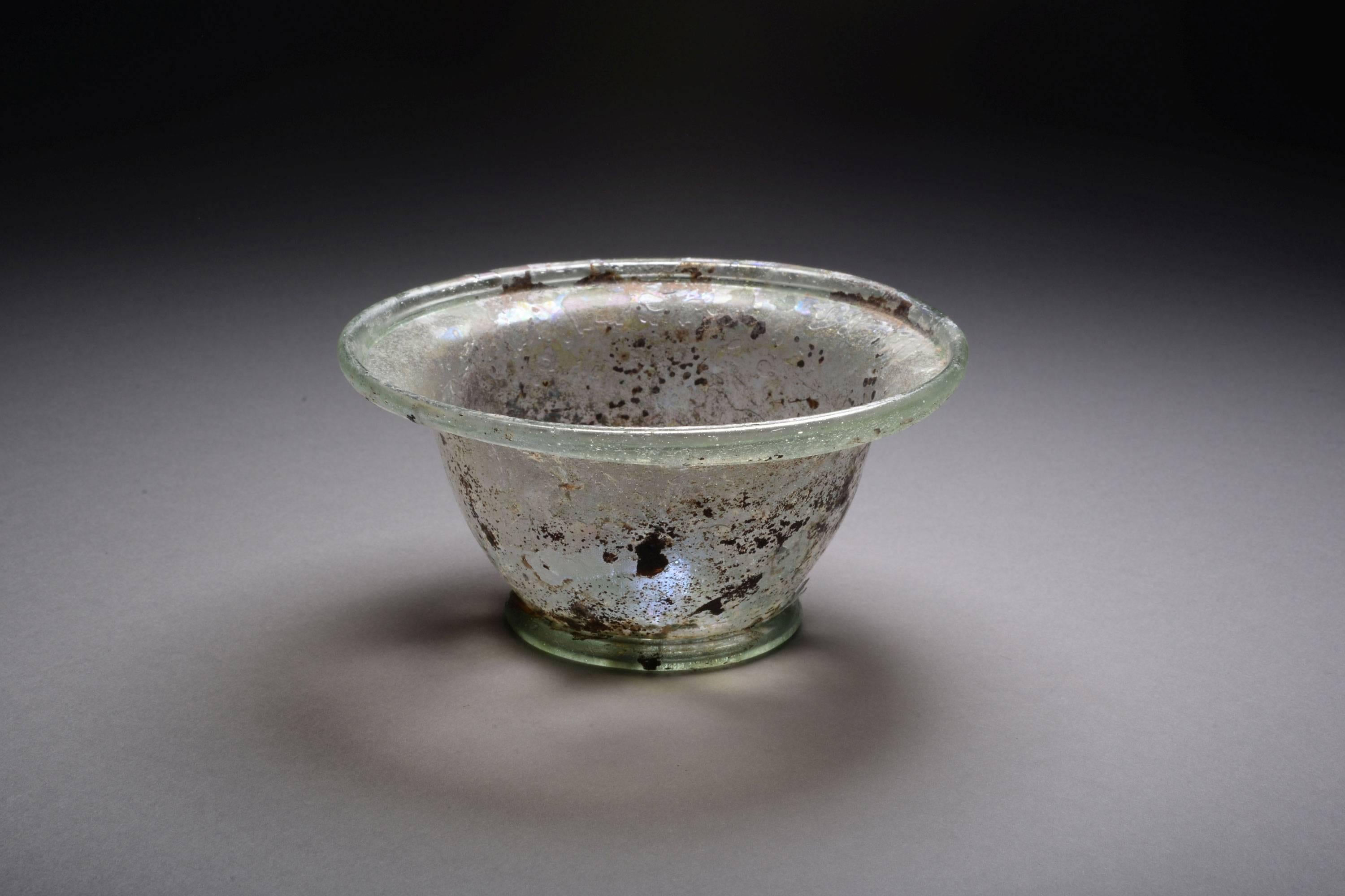 An ancient Roman glass patella cup, dating to the 2nd – 3rd century AD.

Free blown of beautiful light blue glass, the bowl hemispherical, rim outsplayed, with a flattened tubular lip made by folding up and down, sitting upon a ring base with a