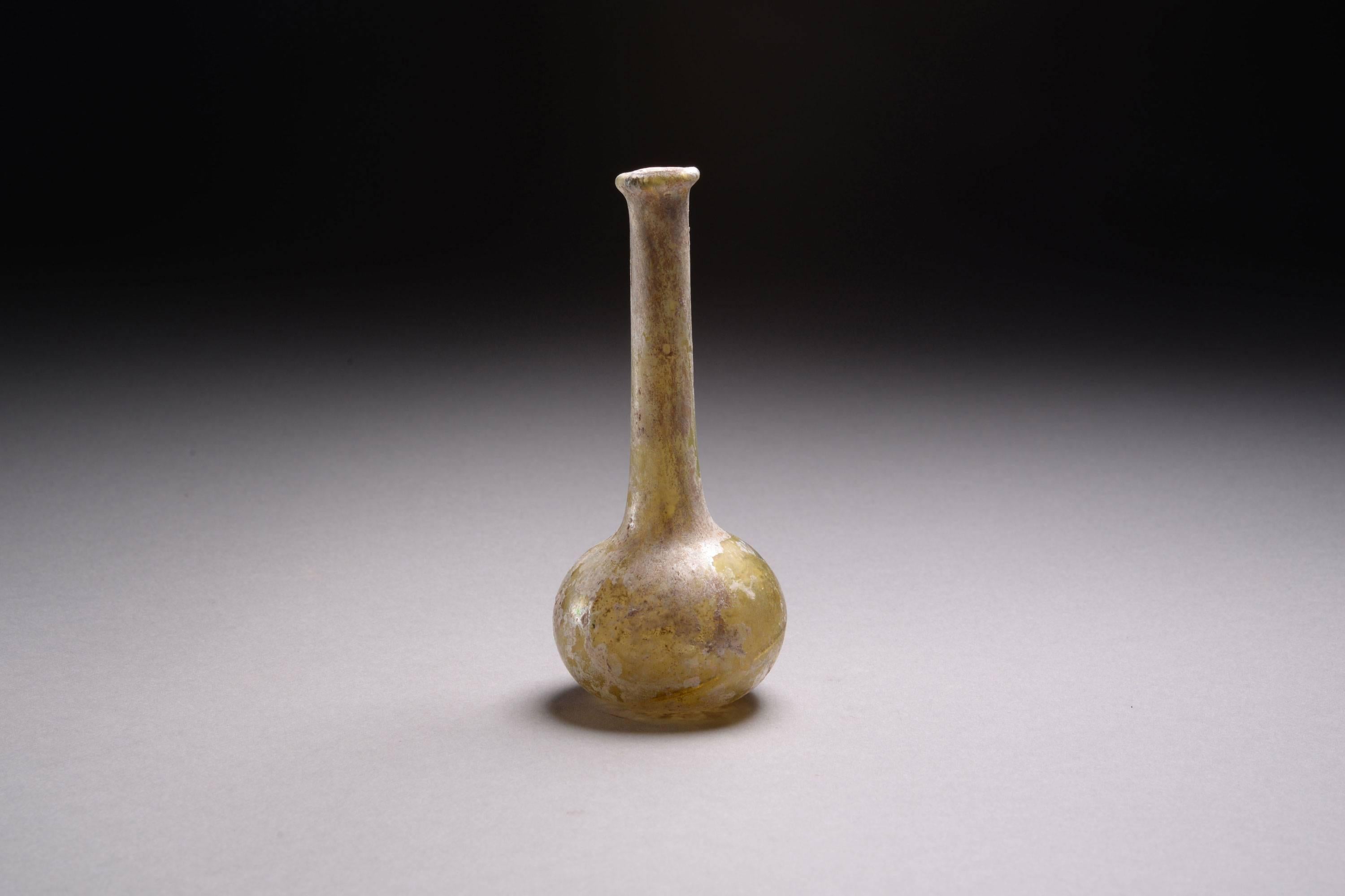 A rare Roman yellow glass unguentarium, dating to the 2nd century AD.

Free blown, the colour a wonderful light yellow, the round body sitting upon a flat base, the long thin neck rising to a rounded lip.

With the long neck cleverly designed so