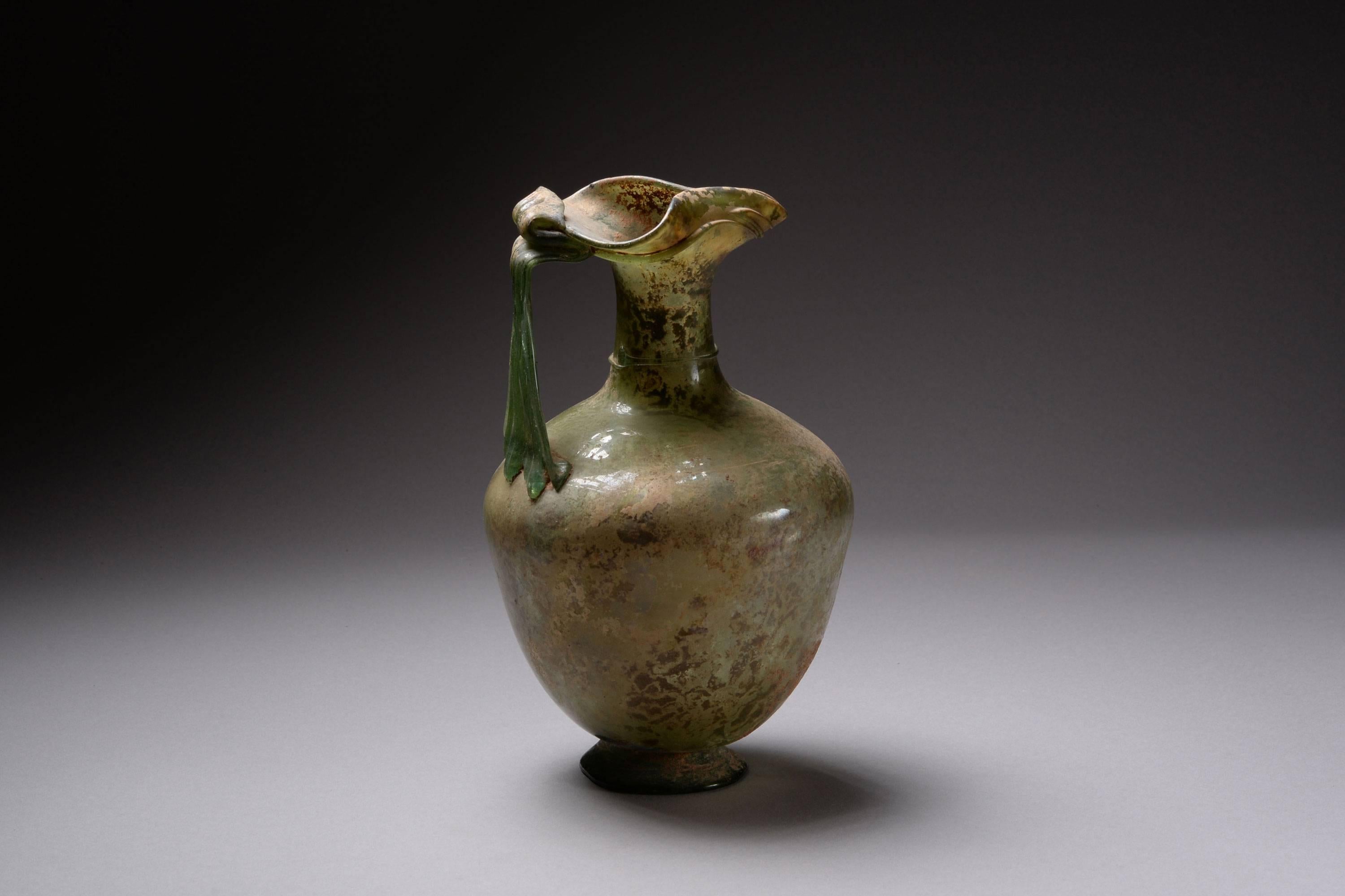 An exceptional, large Roman glass oinochoe or jug, dating to the 3rd to 4th century AD.

Here we see one of the most elegant and refined vessel shapes found in ancient glass.  Free blown, of light green-blue colour, sitting upon an outsplayed