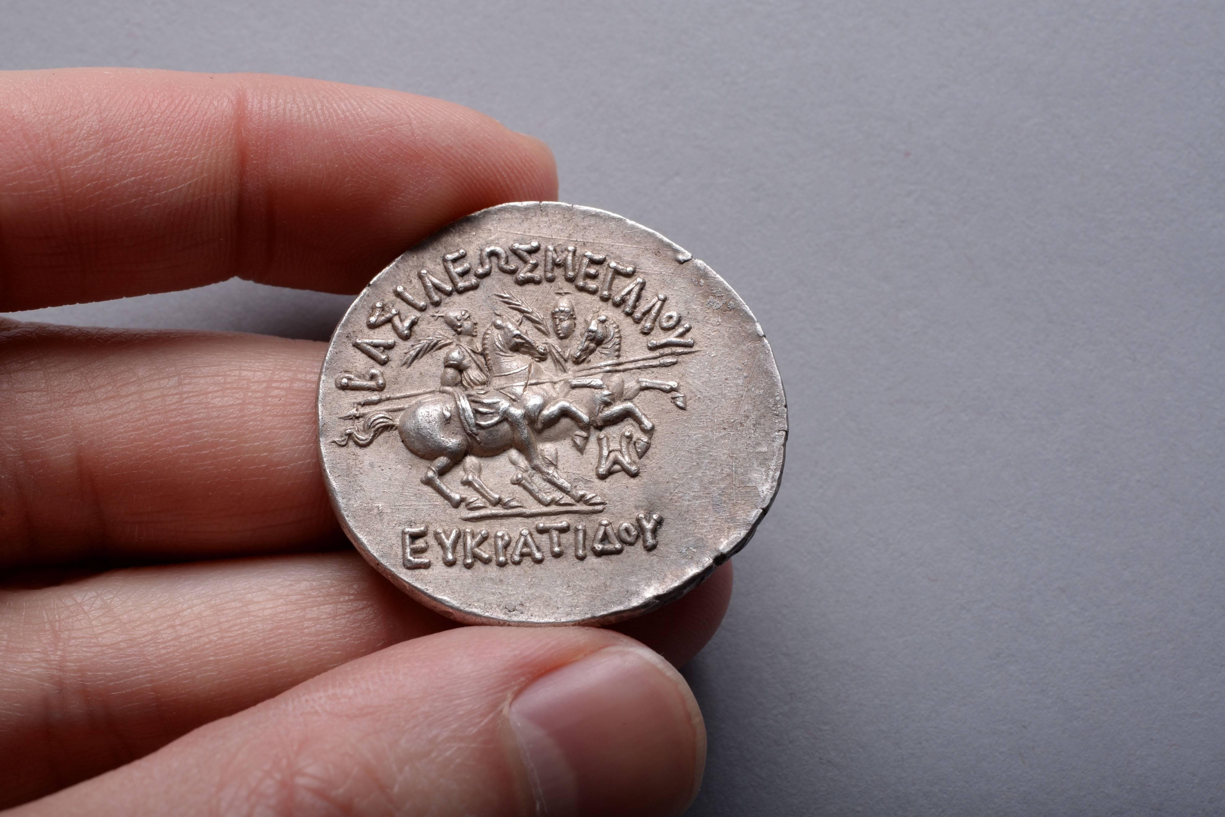 A large, medallic coin minted by the Bactrian King, Eukratides the Great, circa 170-145 BC.

The obverse with a bold portrait of Eukratides, shown as a chubby boy, with a round chin, plump cheeks and slightly parted lips. The young King is dressed