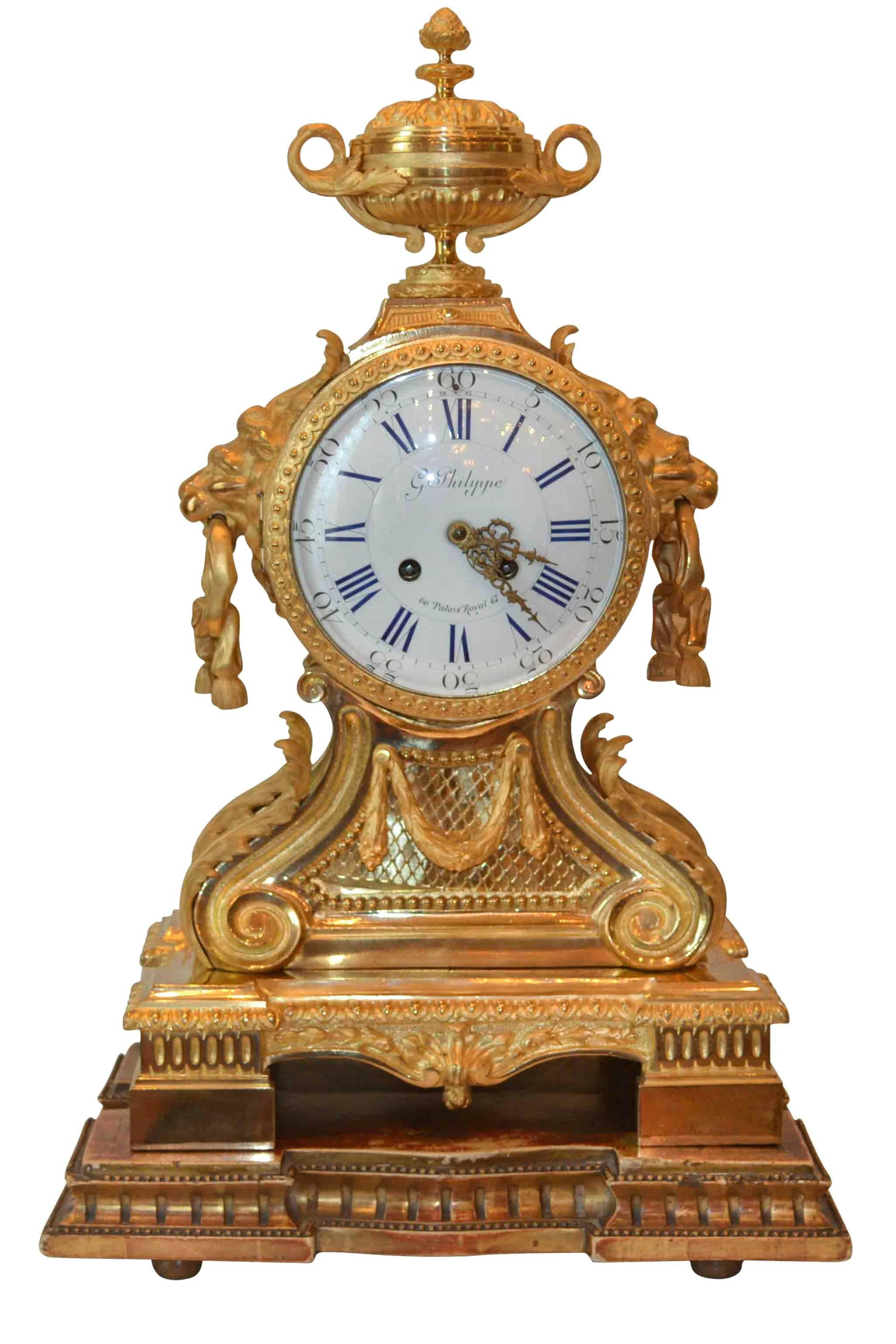 A gilt and chiseled bronze lion's head mantel clock with lion's head masks and decoration of interlacing frieze, laurel leaf cascades, cross-bars and acanthus leaves. Surmounted by a flambeau urn, the whole atop plinth with four feet.

White