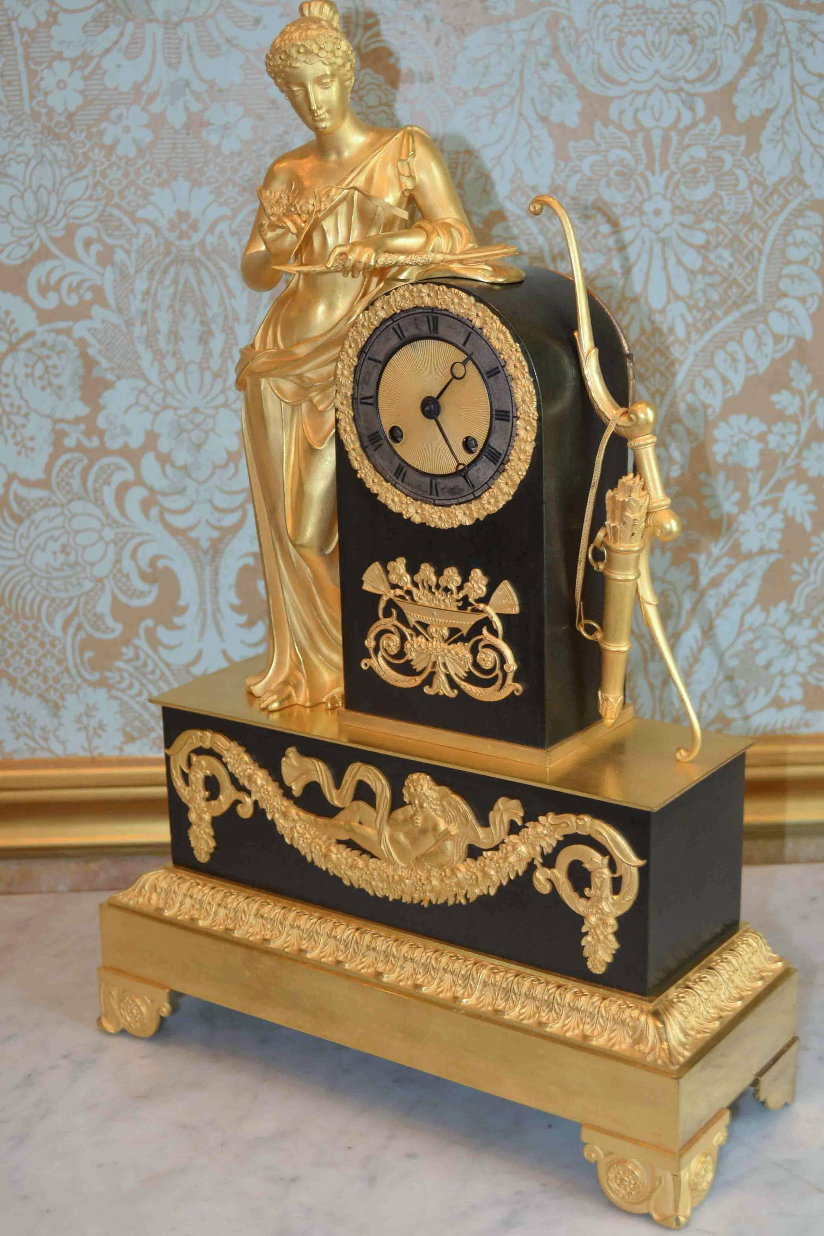 Patinated and gilt bronze Empire clock with a standing Psyche or Venus unravelling her arrows. She stands beside a patinated plinth housing the clock movement with a bow and quiver leaning against it. The lower rectangular base, also of patinated