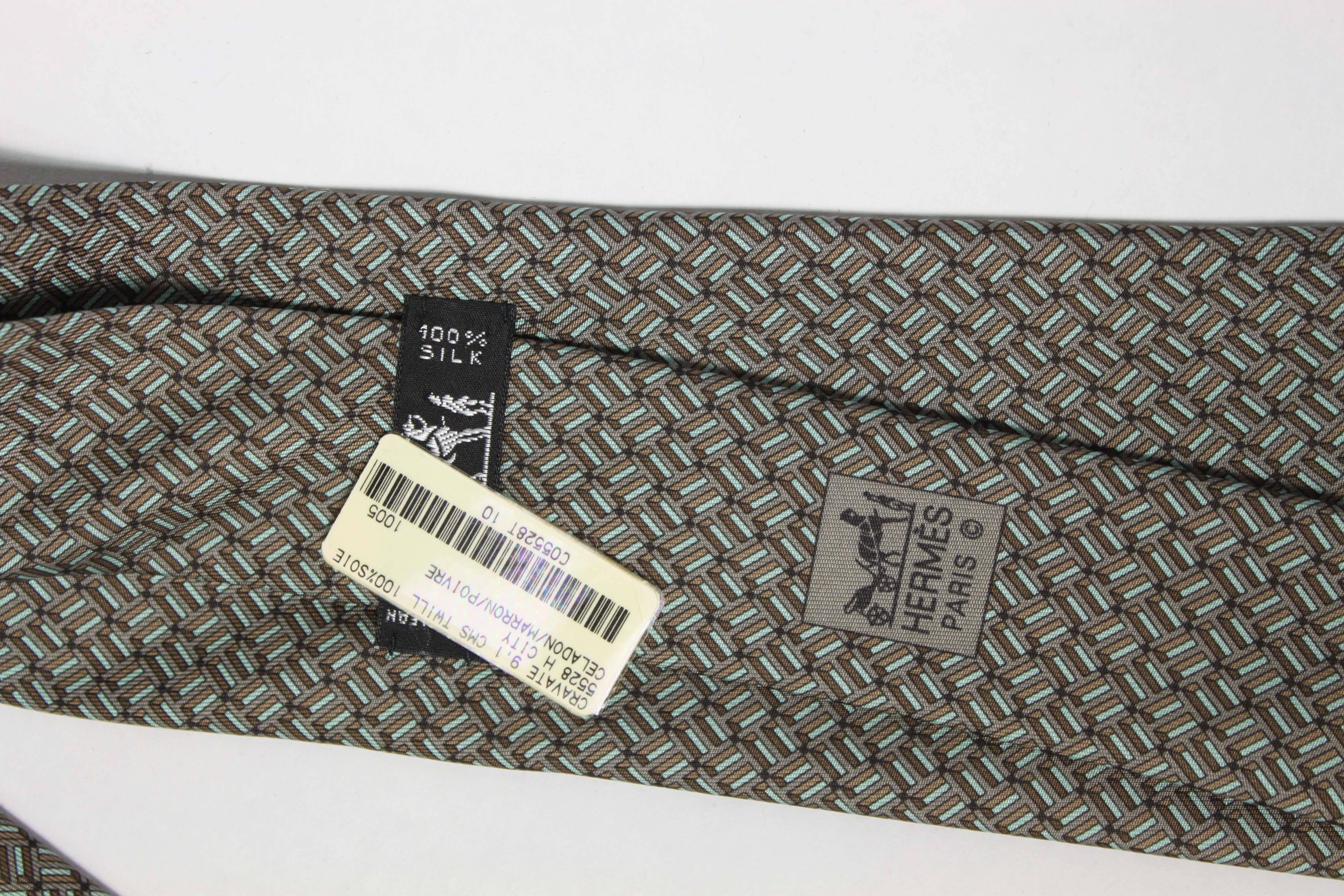Hermès silk tie in tones of grey and green. Includes original tag, never worn, packaging not included.