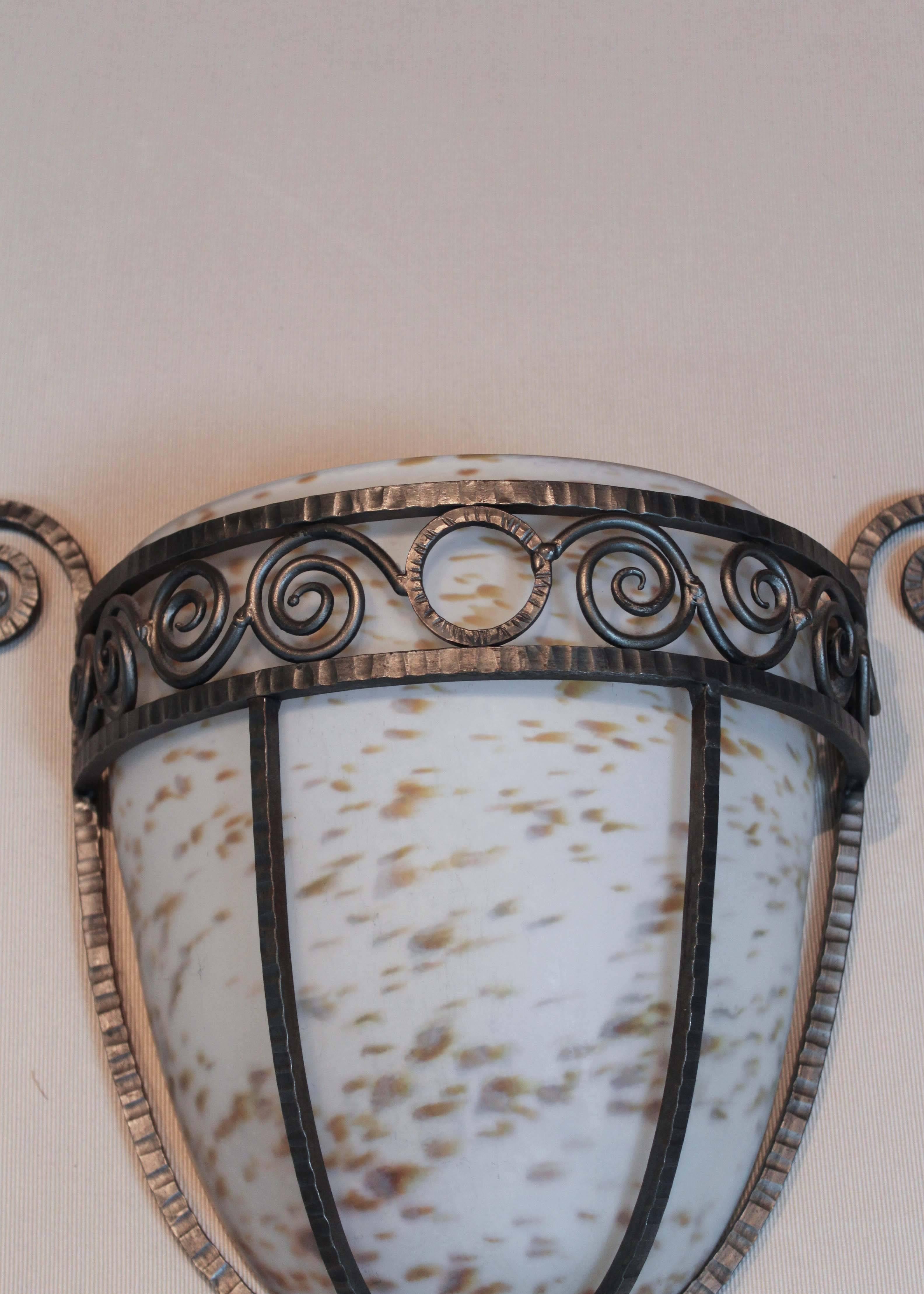 Set of eight hammered wrought iron sconces with speckled milk glass inserts in the style of William Haines. These sconces are not wired, they are meant to be decorative pieces mounted over an existing light source.

The set of eight is comprised