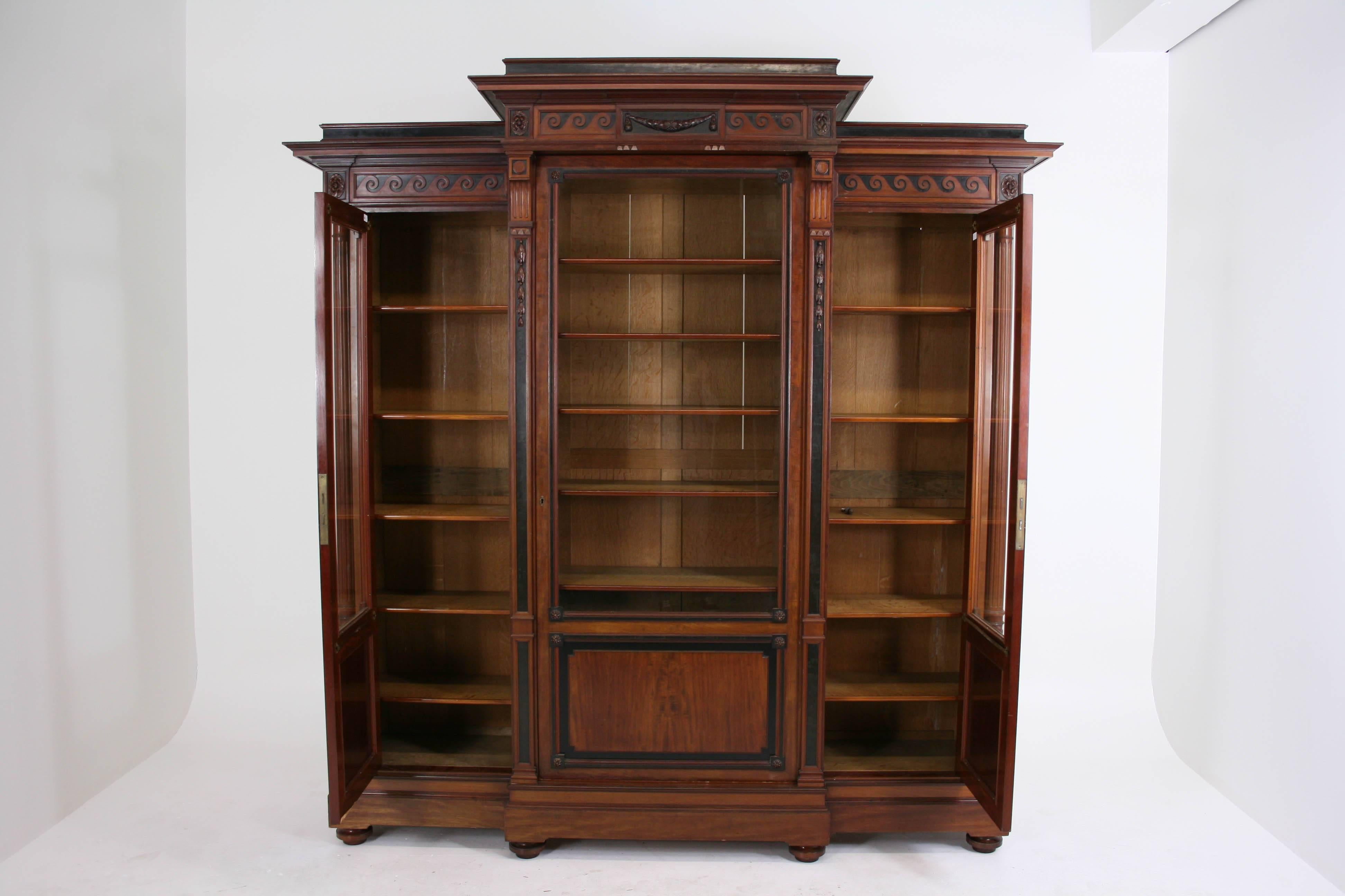 Solid mahogany bookcase with original finish and stepped-back cornice. A beautiful piece exhibiting carved scrolls, laurel swags, fluted/turned columns and tiger oak adjustable shelves. Sits on plinth with bun feet. Very good original condition.