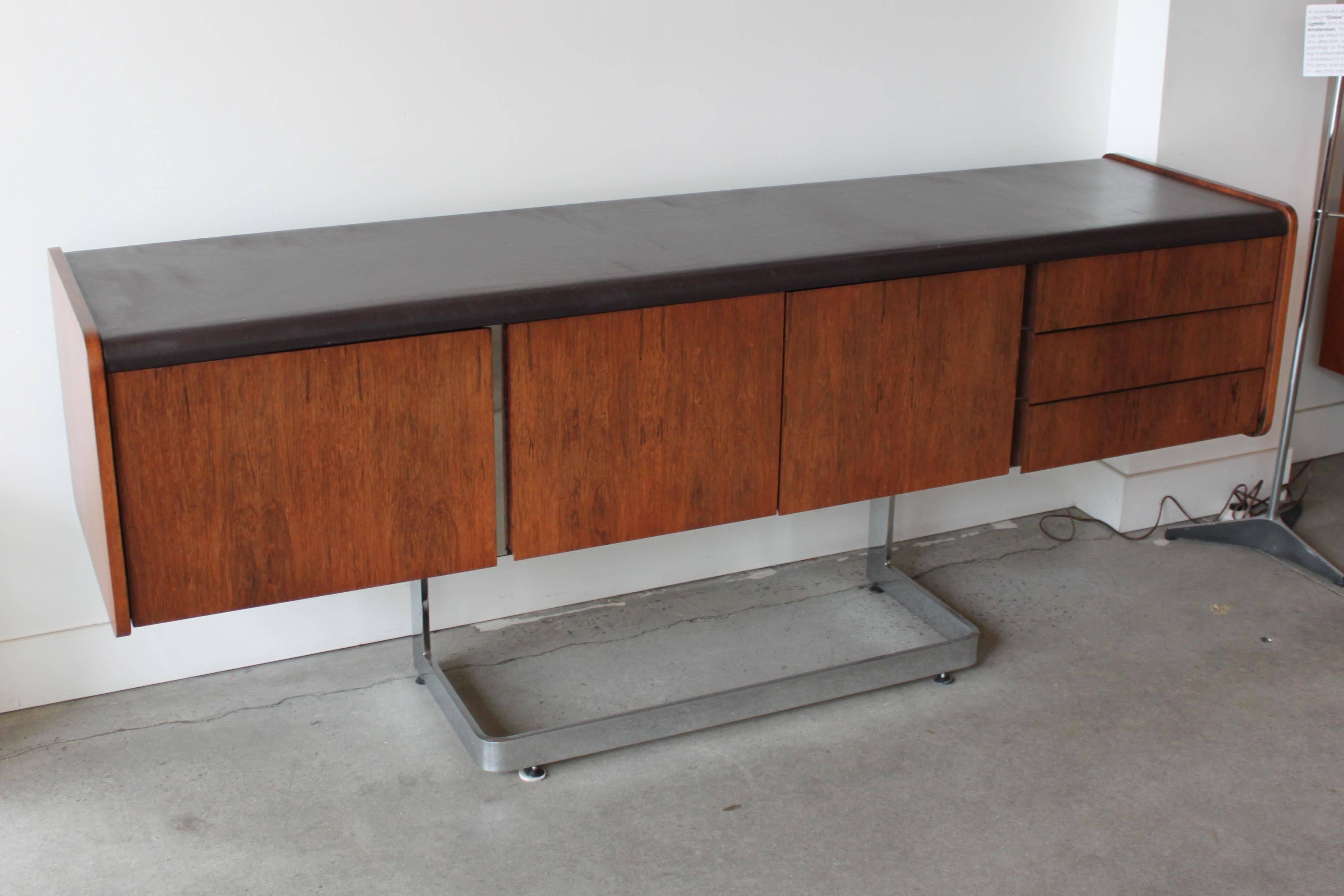 A beautiful credenza by Ste. Marie and Laurent with black leather top, deep file drawer, three single drawers and center storage cabinet. The whole is cantilevered onto a polished chrome base. In good original condition with minor wear consistent